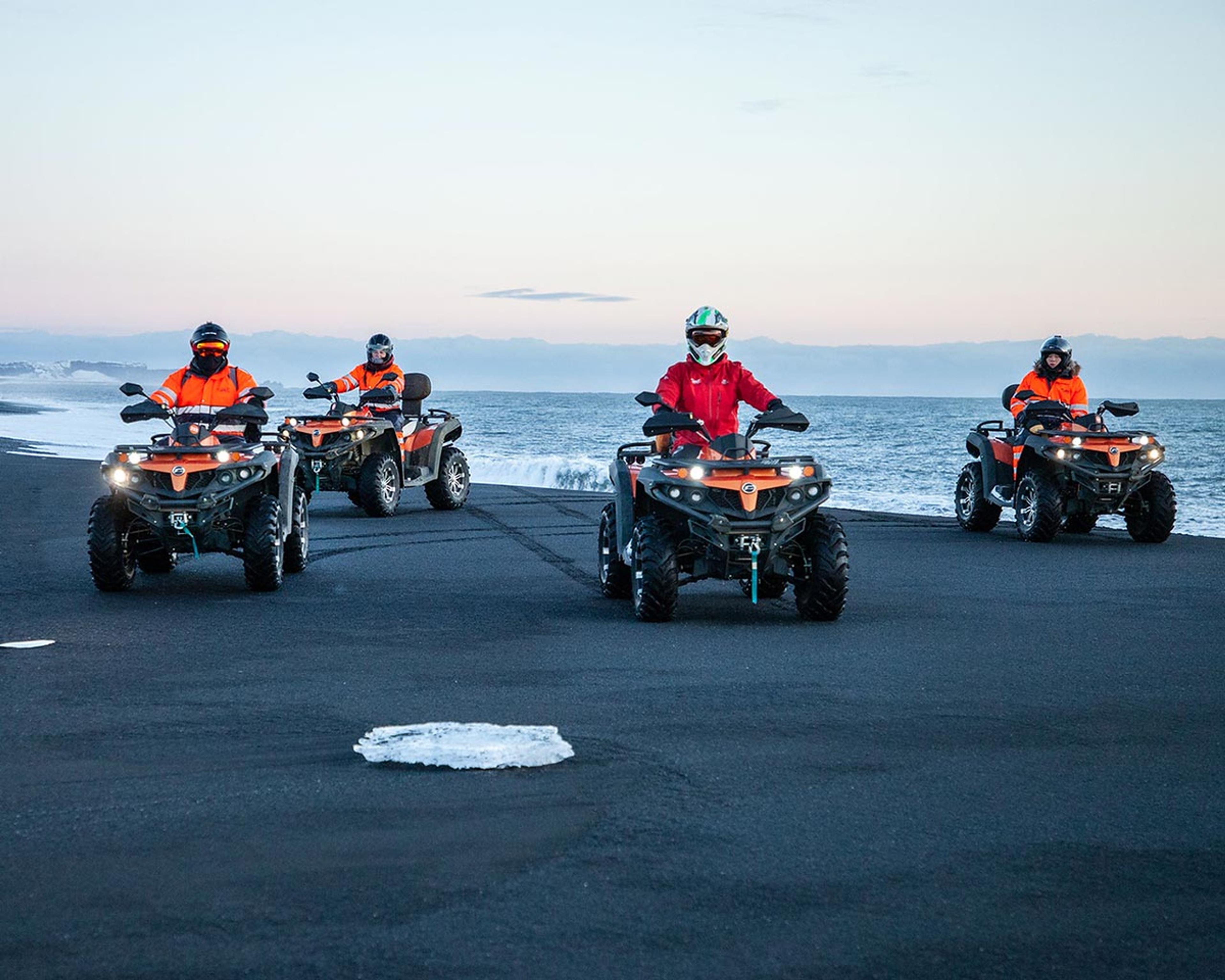 Four ATV quad bikes and drivers posing on the black sand beach