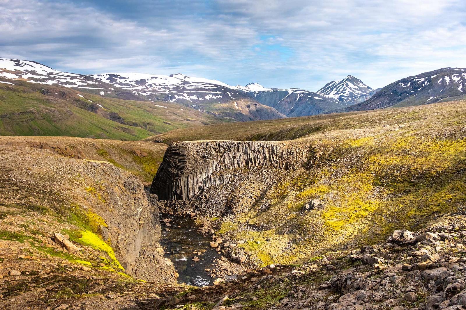 Basal column rock formations and a river creek flowing by with mountains in the distance
