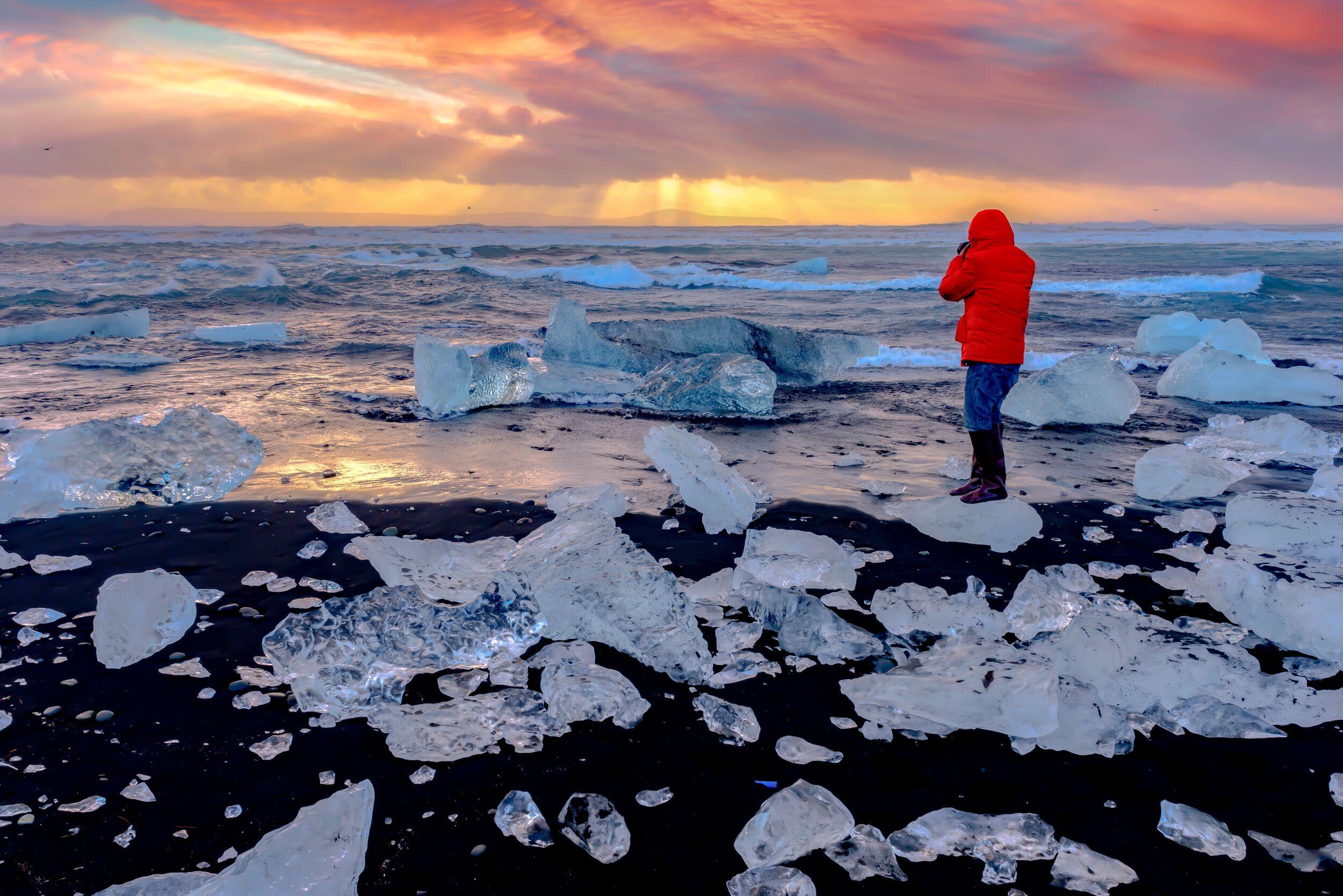 A person in a red coat admiring the glacier breakoff on Diamond Beach in Iceland at sunset