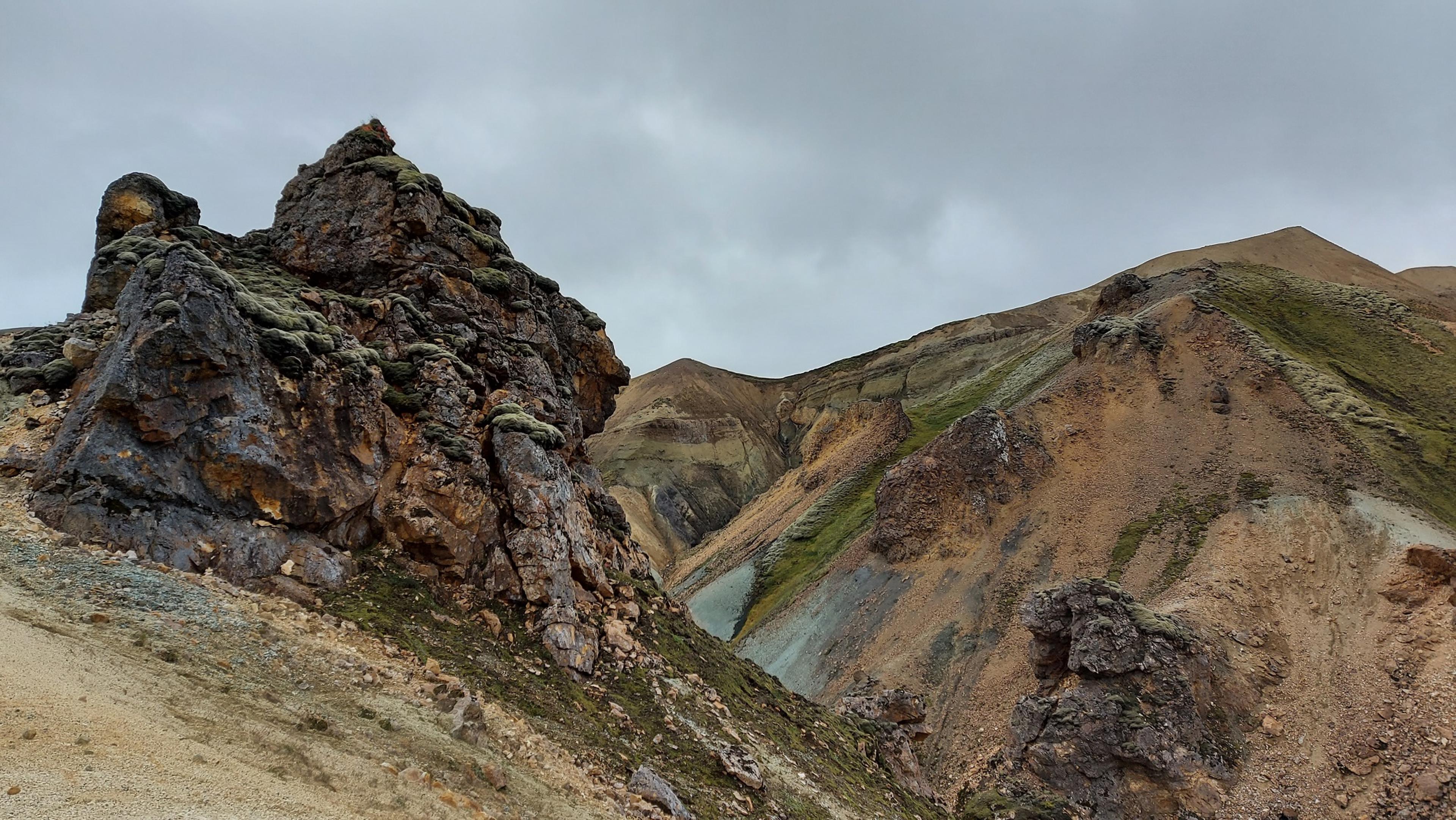 Jagged volcanic rocks and colorful slopes create a dramatic landscape under a gray sky in Landmannalaugar.