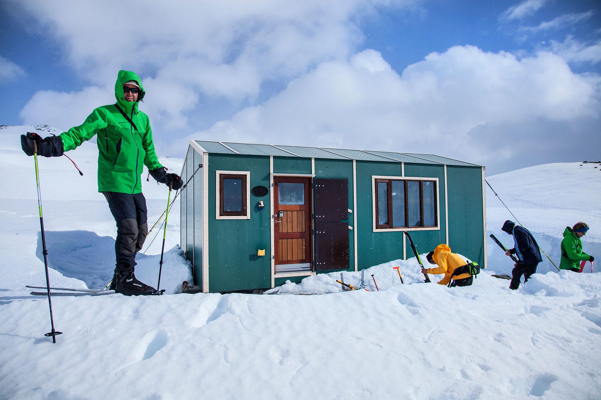 A skier standing in front of the Esjufjöll mountains hut and some others there in the background