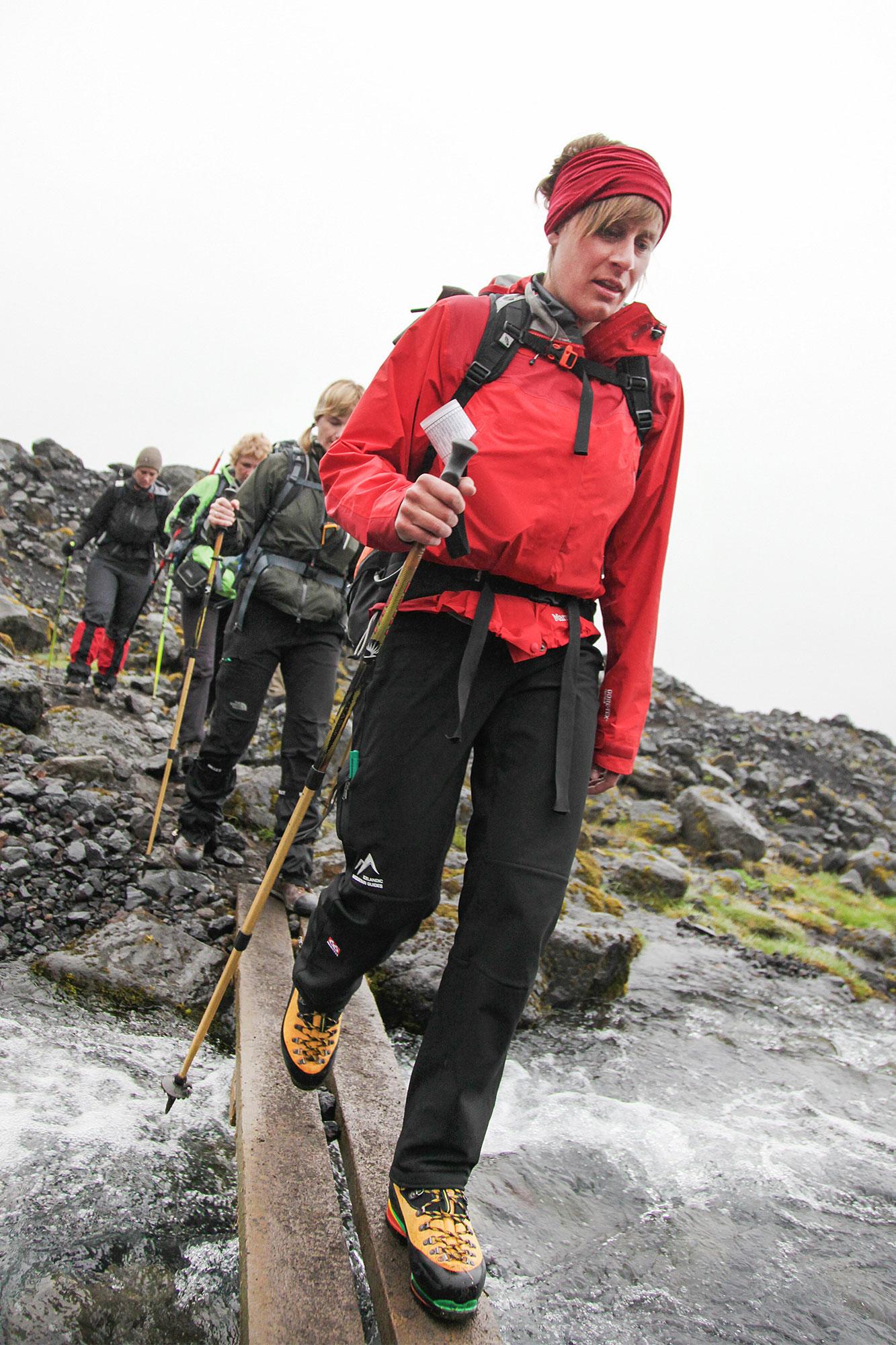 A guide from Icelandic Mountain Guides leading a group across a narrow wooden bridge.