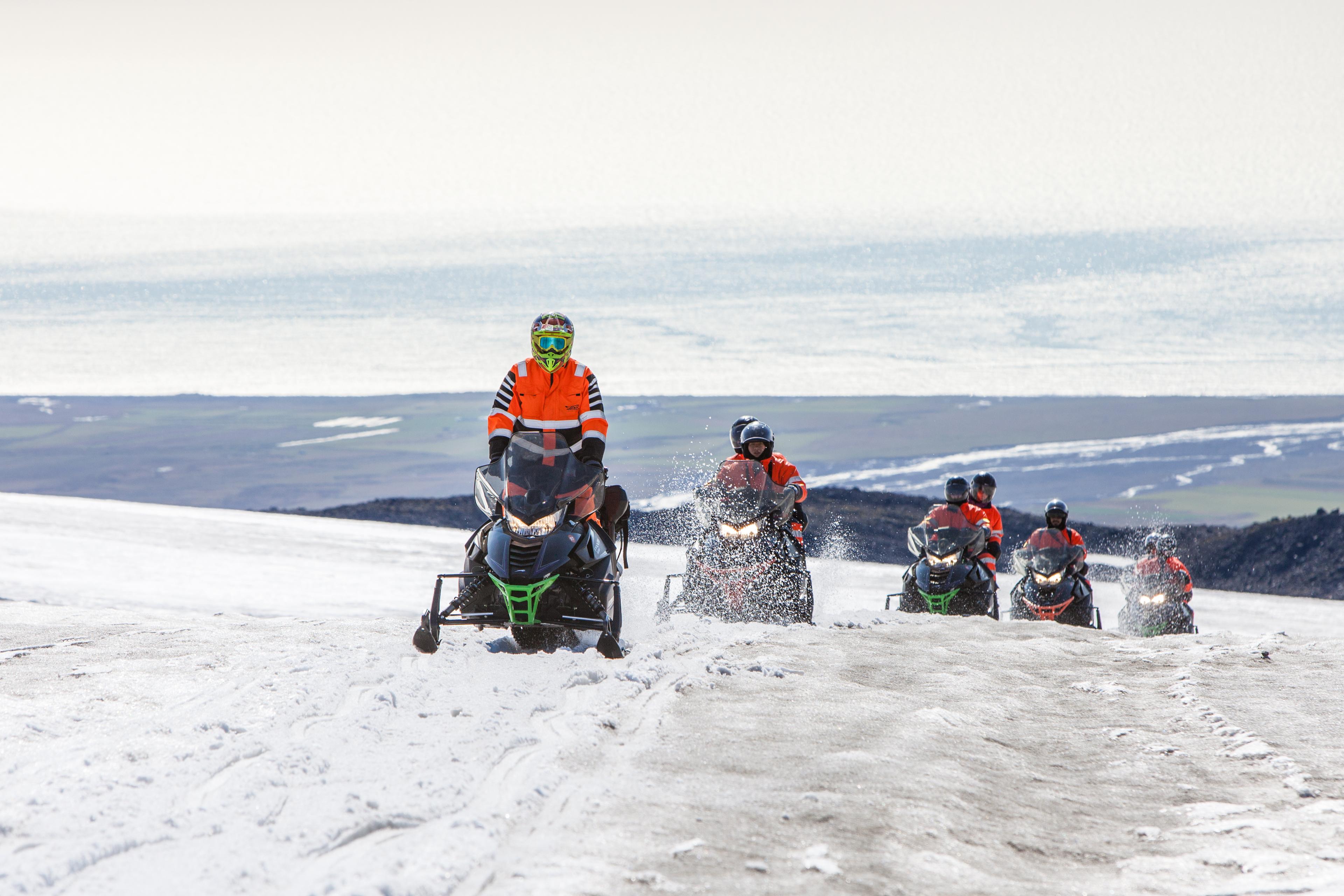 Snow scooter riders going higher up on the glacier with a ocean view in the background