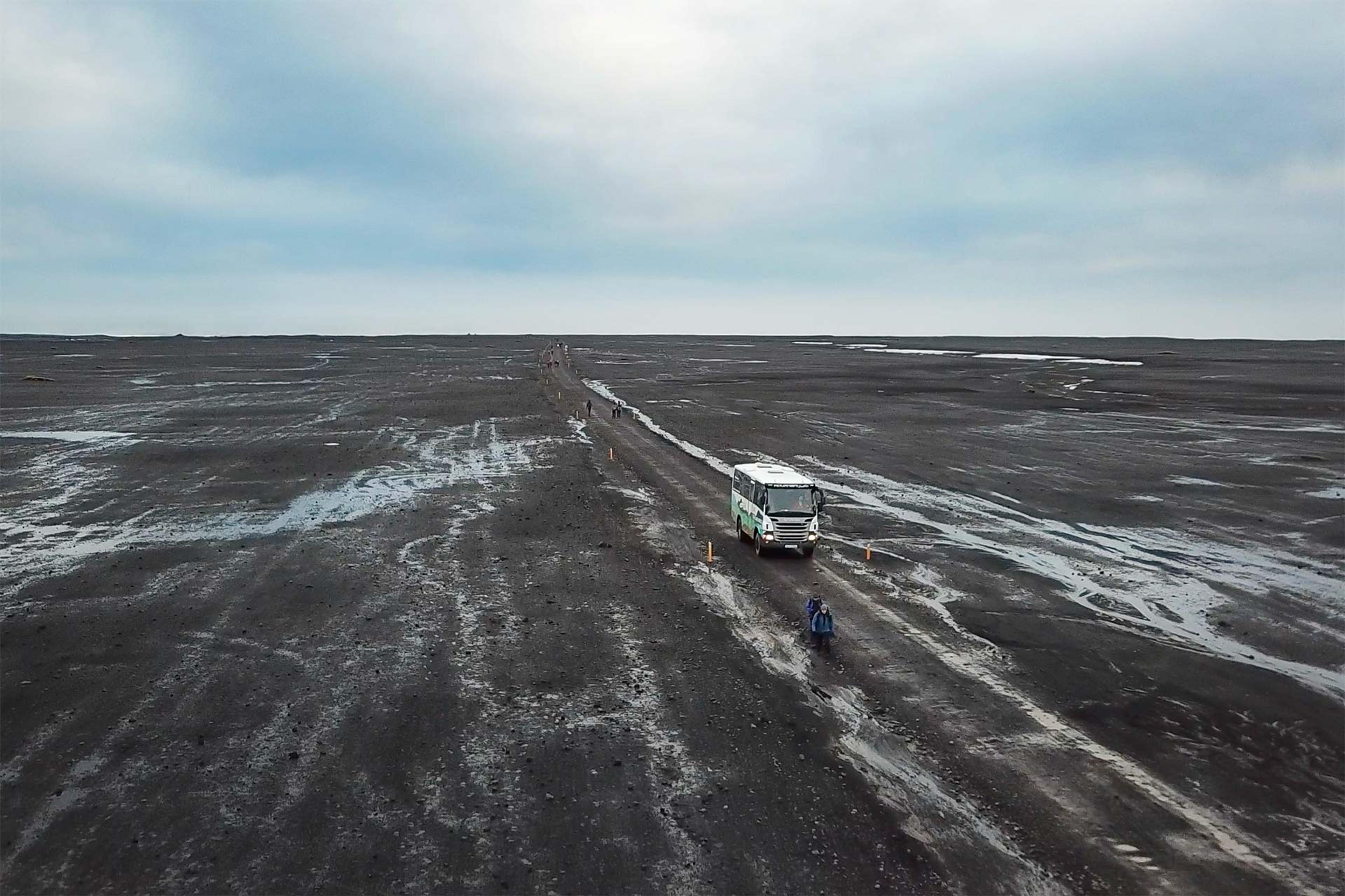 bus driving through black sand dessert looking nature under blue sky