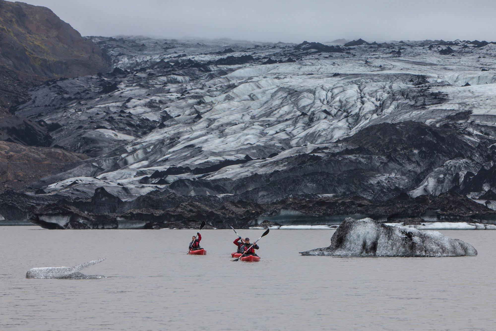 People kayaking on a glacier lagoon by Sólheimajökull glacier that is seen in the background