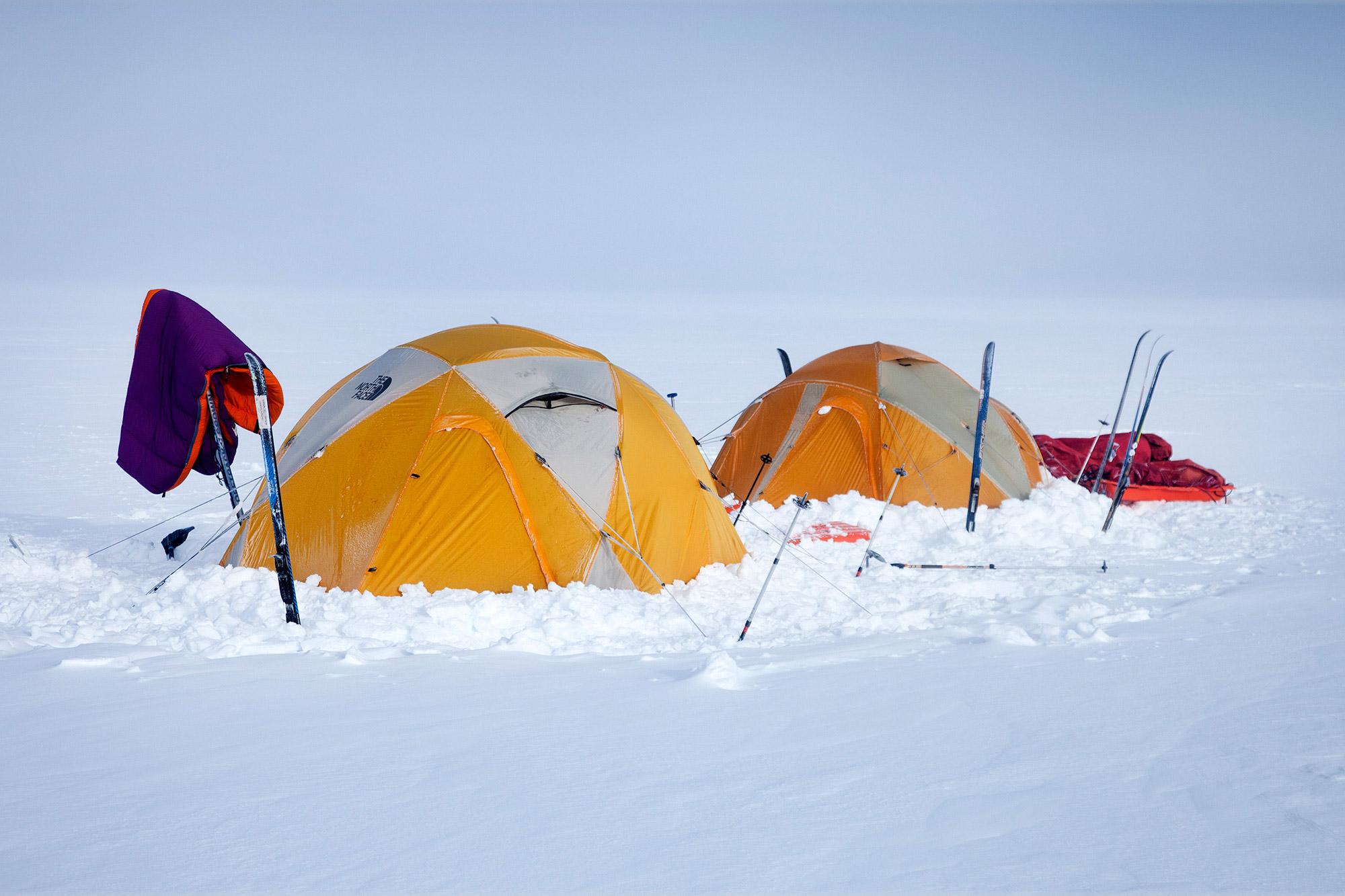 Two tents in the snow and a sleeping bag being dried on on of the skis