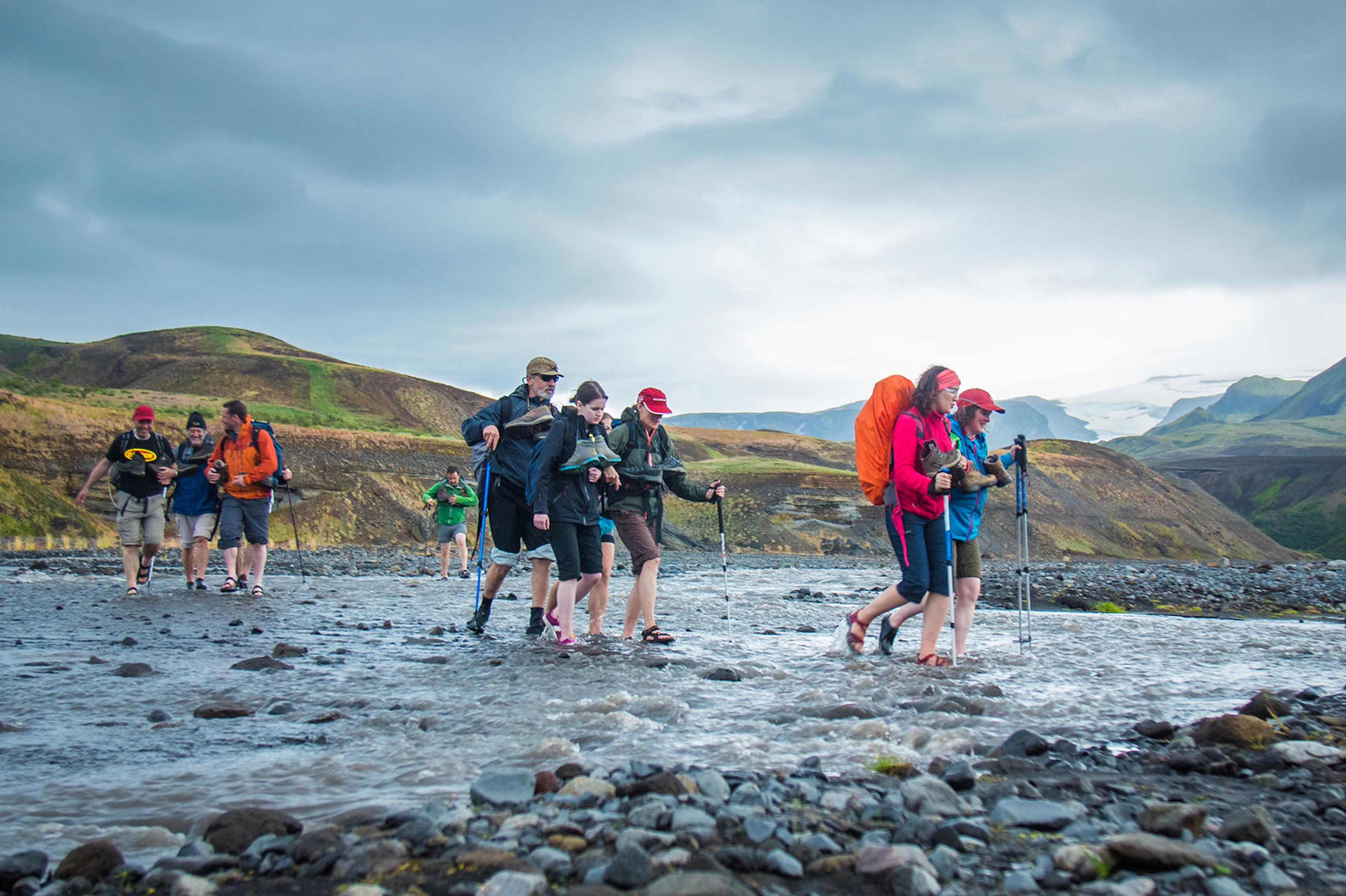 People river crossing a blue lake as they hike the Laugavegur trail on a cloudy day