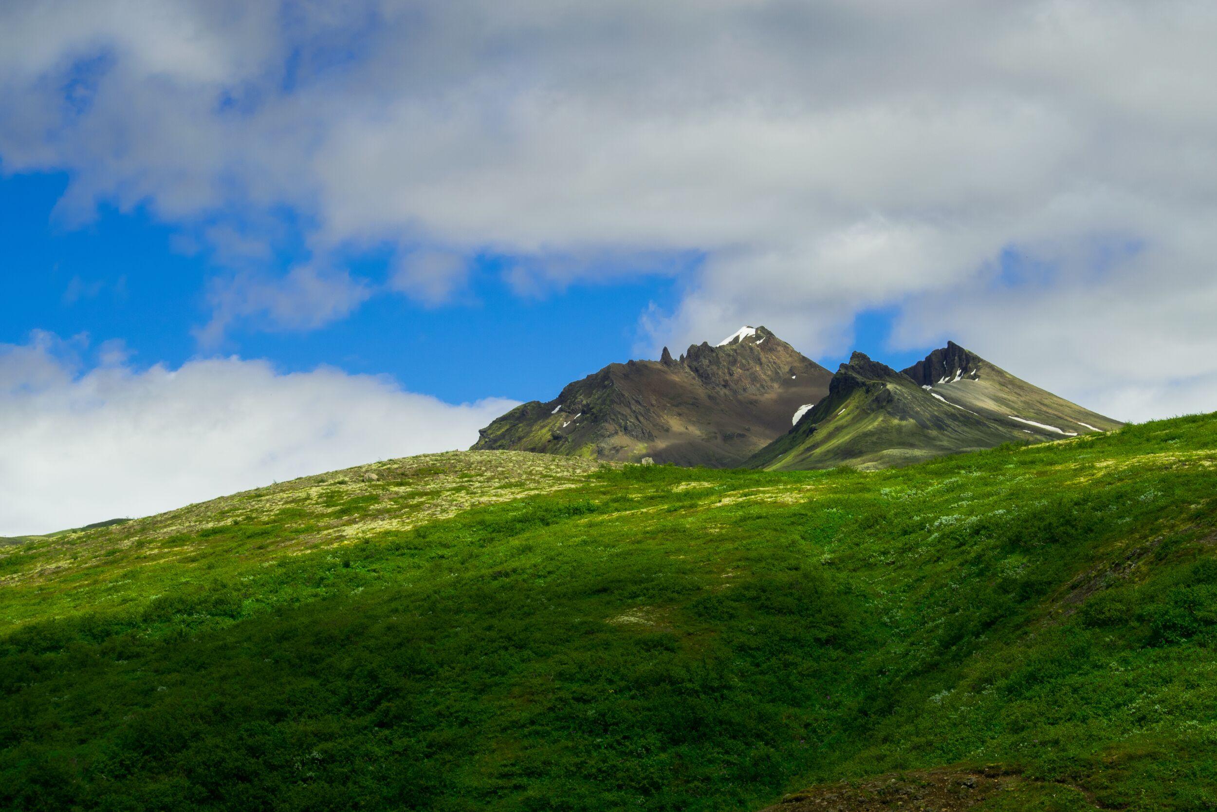 Rugged peaks of Kristínartindar rising above lush green slopes under a partly cloudy sky in Skaftafell, Iceland.