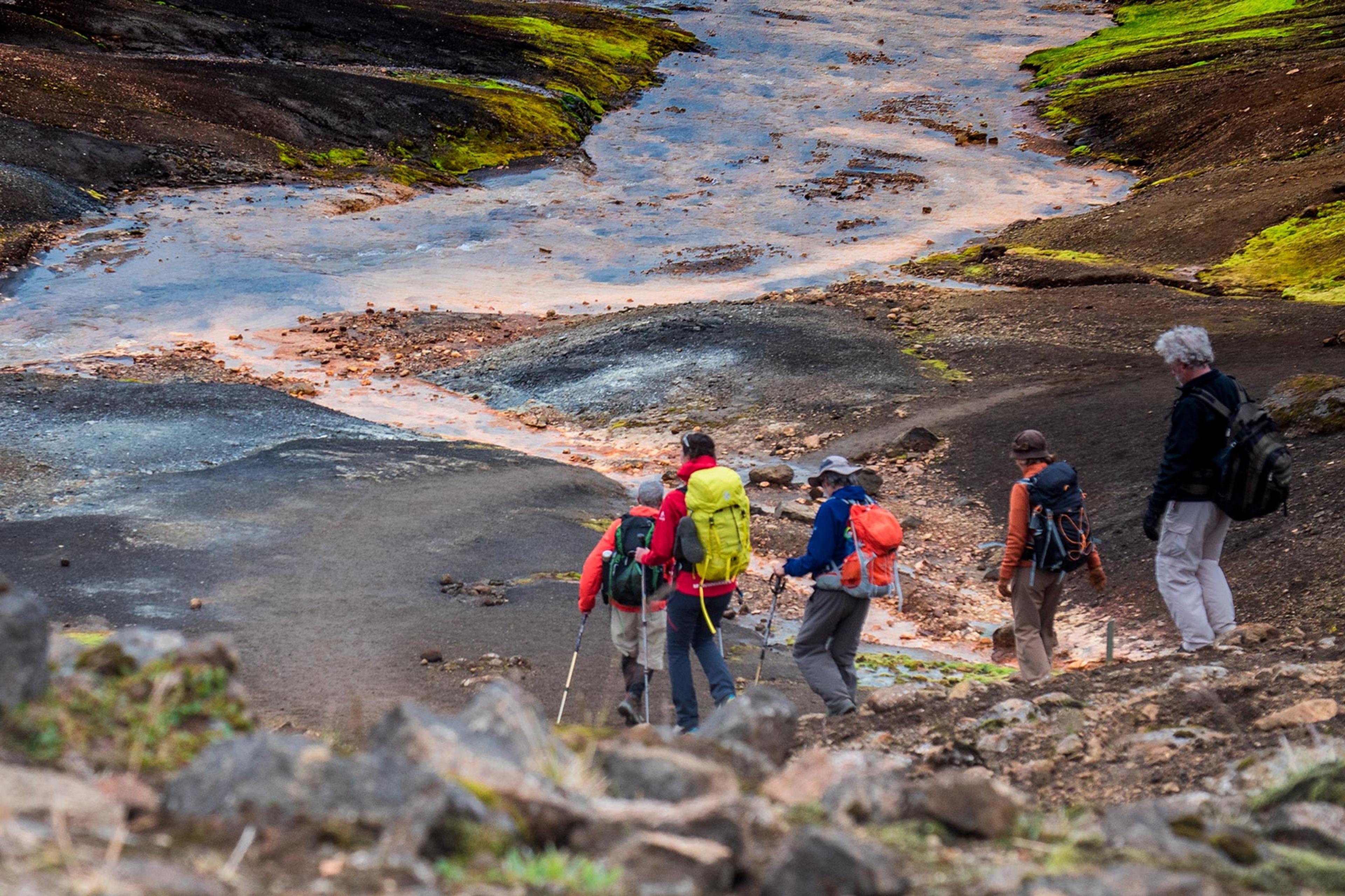 People hiking down a hill on their way to cross a river where the surrounding sand is black and rocks are red