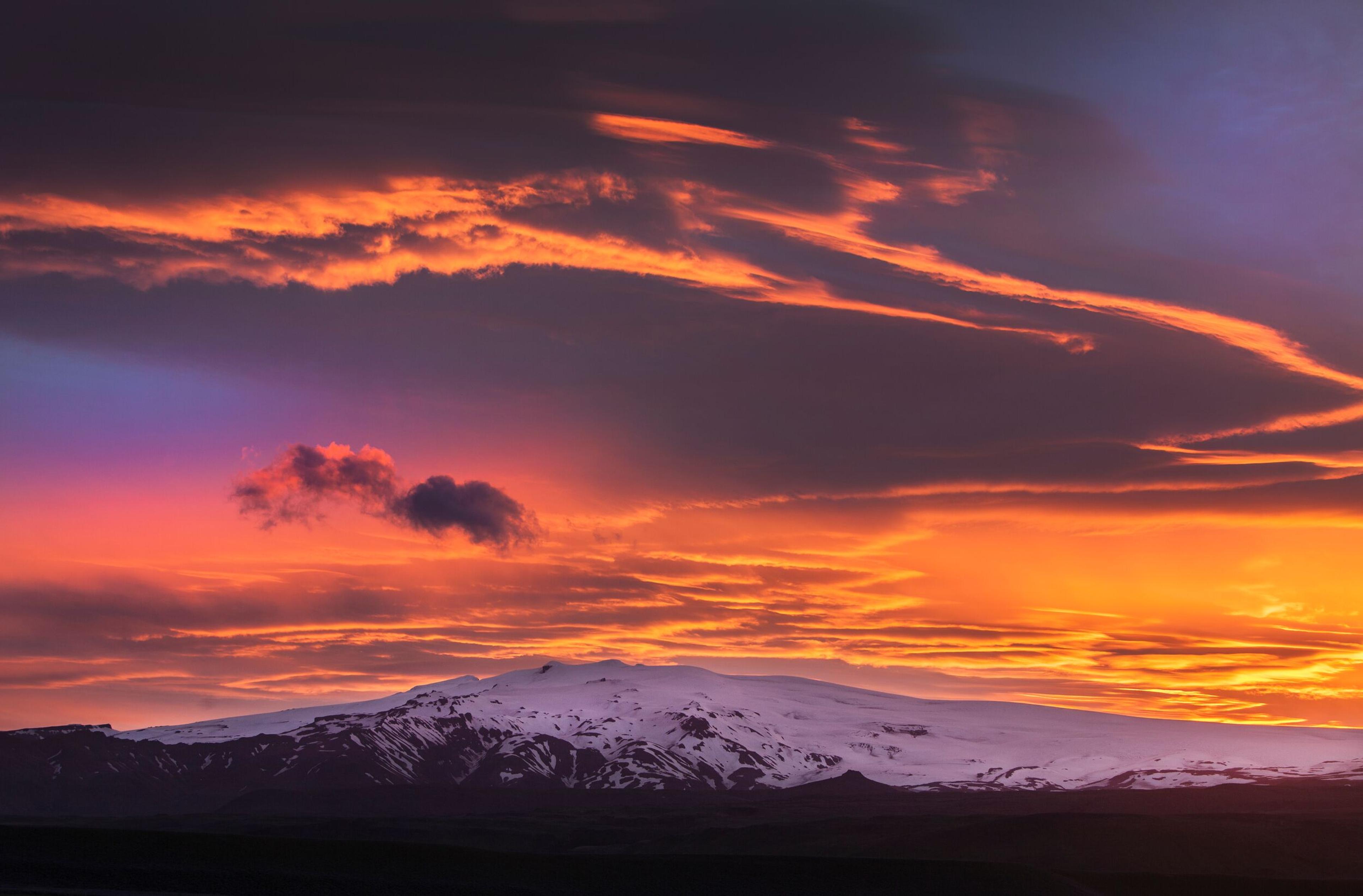 A breathtaking view of Eyjafjallajökull under a dramatic sunset, with vivid orange, purple, and pink hues illuminating the sky above the snow-capped mountain.