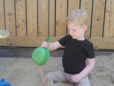 Kind speelt in zandbak met groen bakje