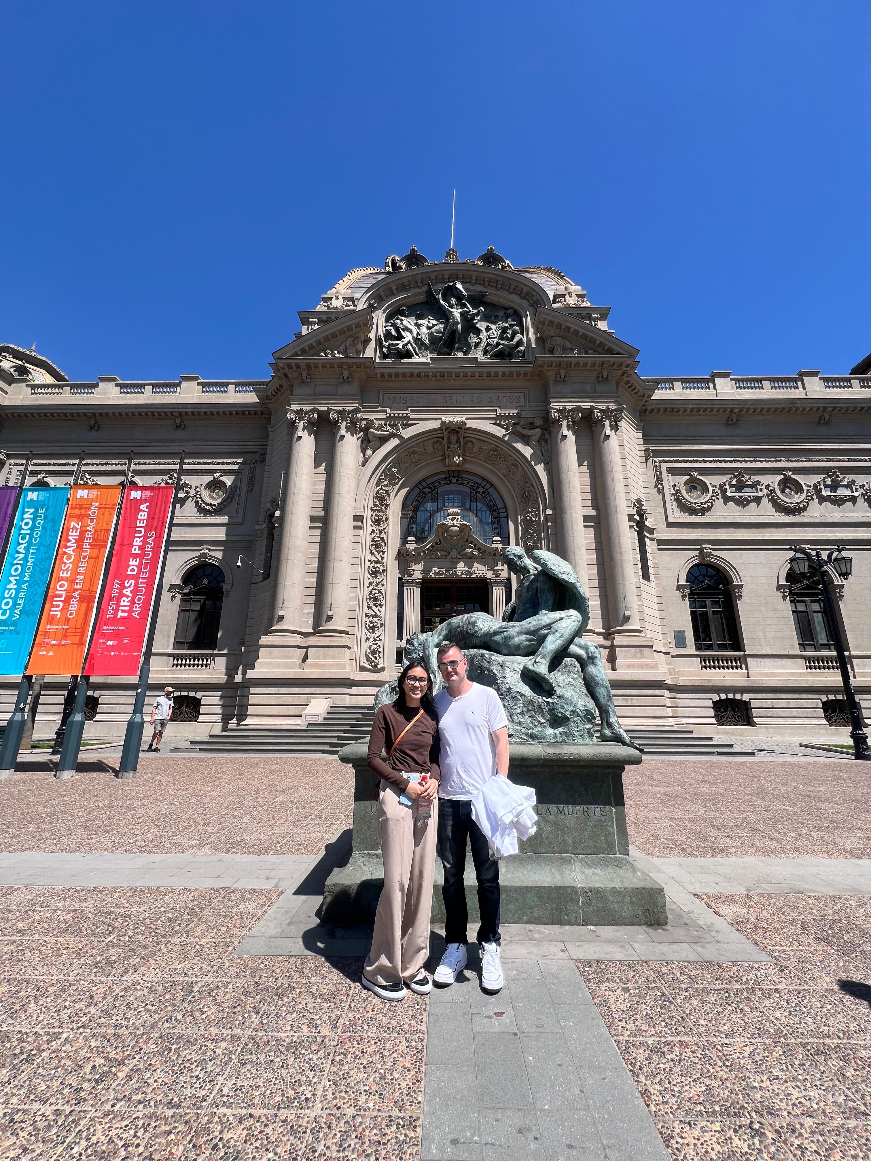 A couple posing in front of the National History Museum, a statue standing beside them
