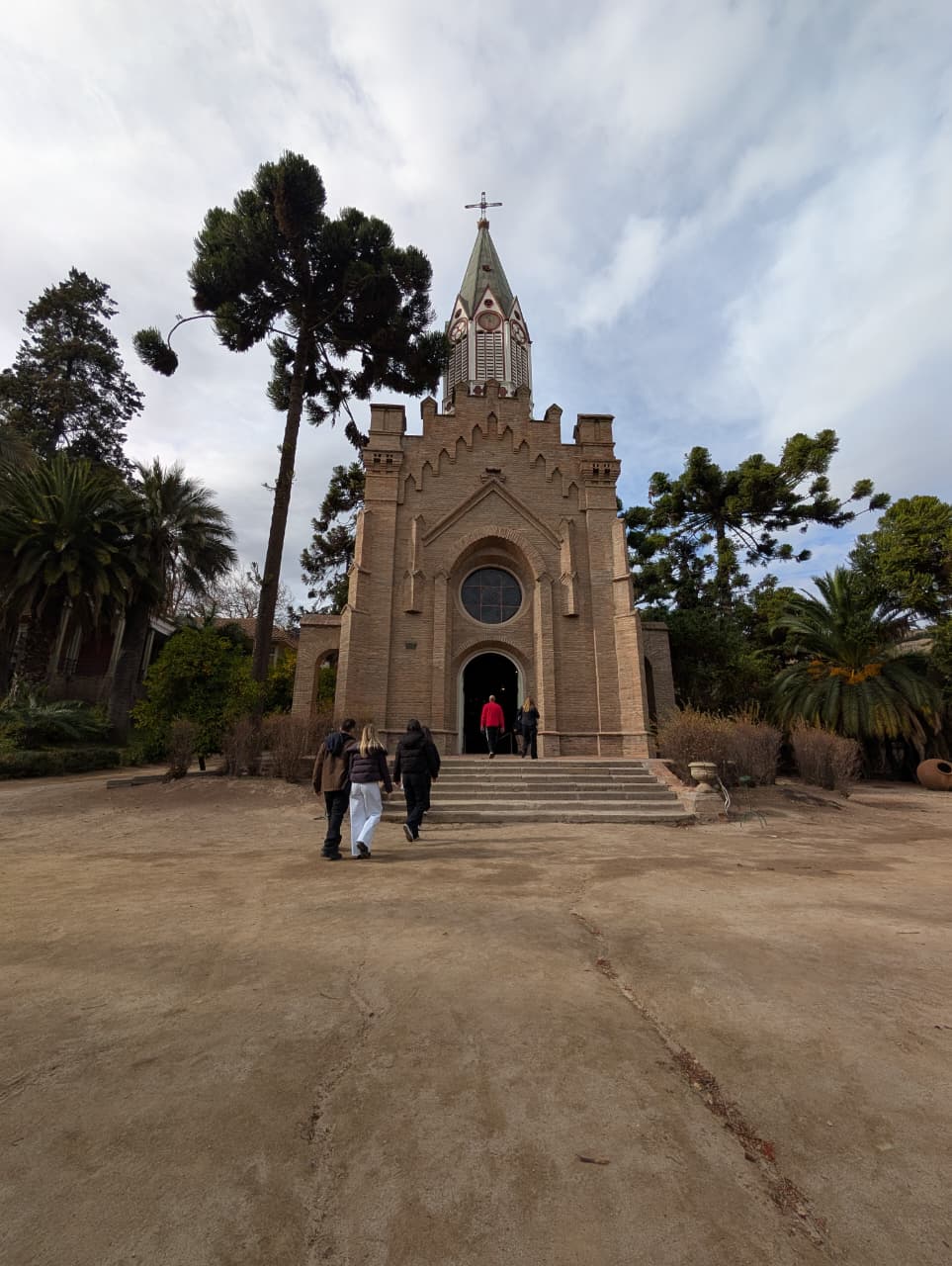 A stone chapel with a bell tower at the end of a tree-lined path