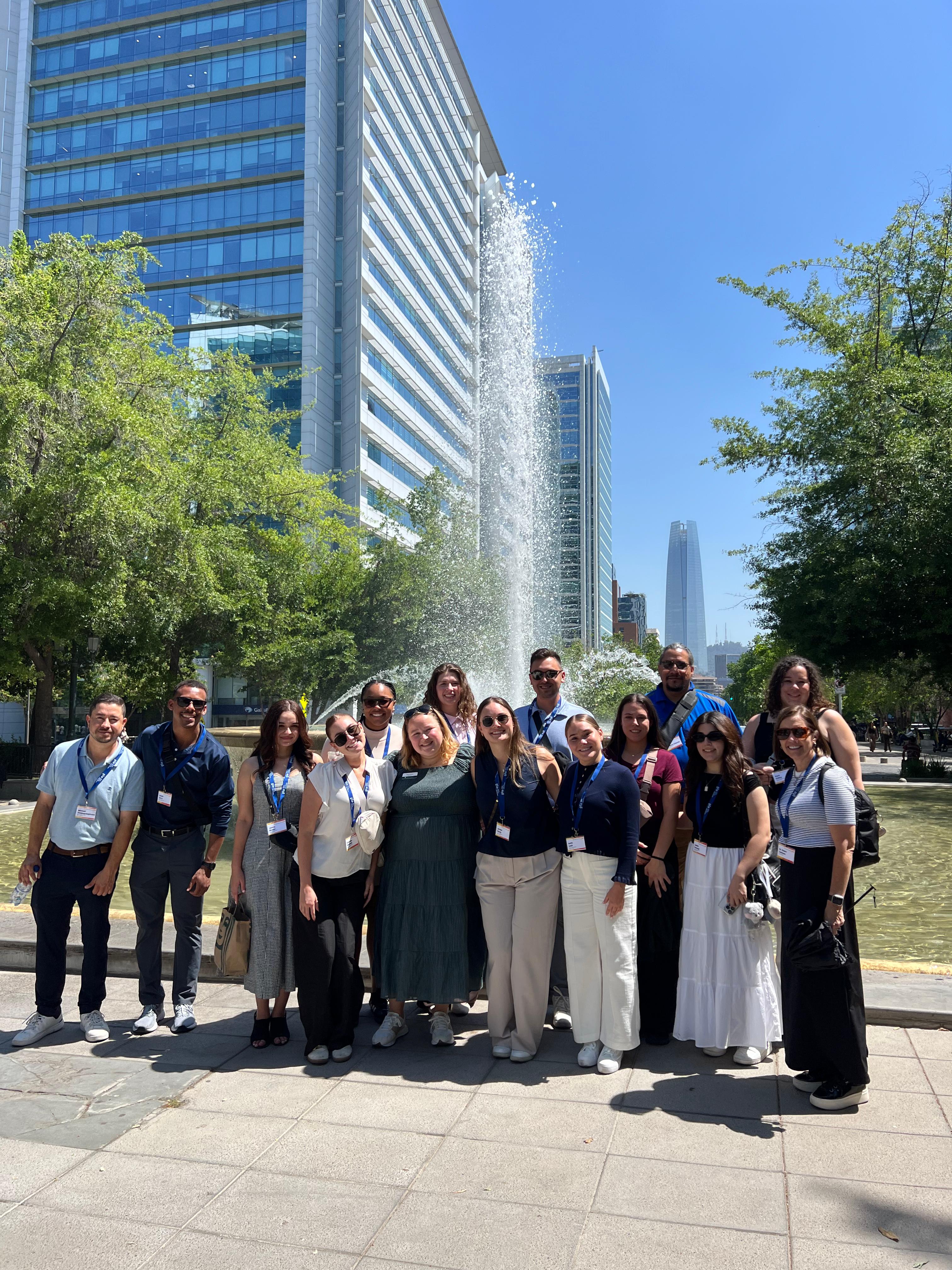 A group posing together on a plaza with the glass office towers of Sanhattan rising behind them