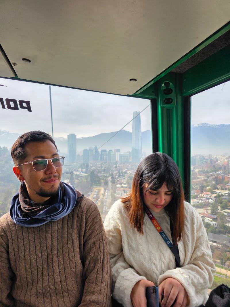 Two passengers inside a cable car cabin with the hazy city skyline behind them