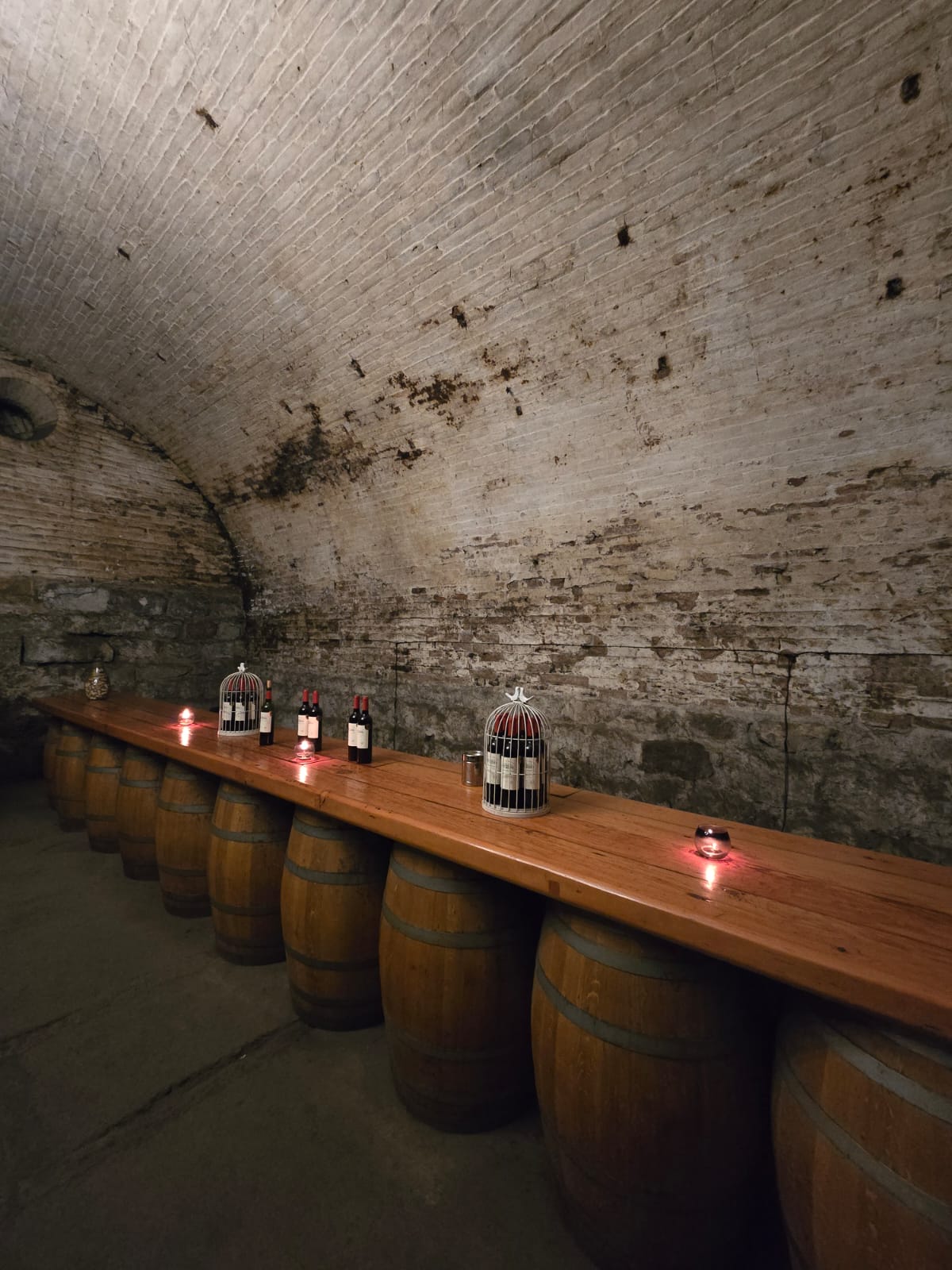 Bottles and glasses of red wine set out on barrels inside the candlelit brick tunnel
