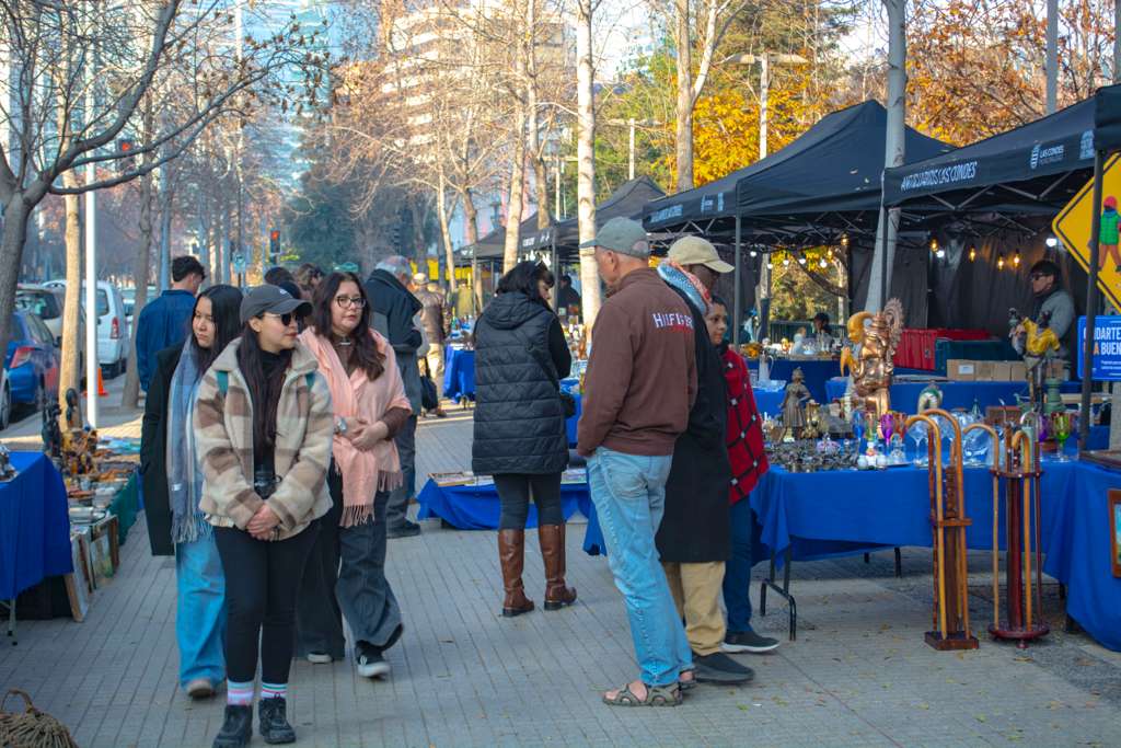 Visitors browsing an outdoor artisan market with blue-tented stalls