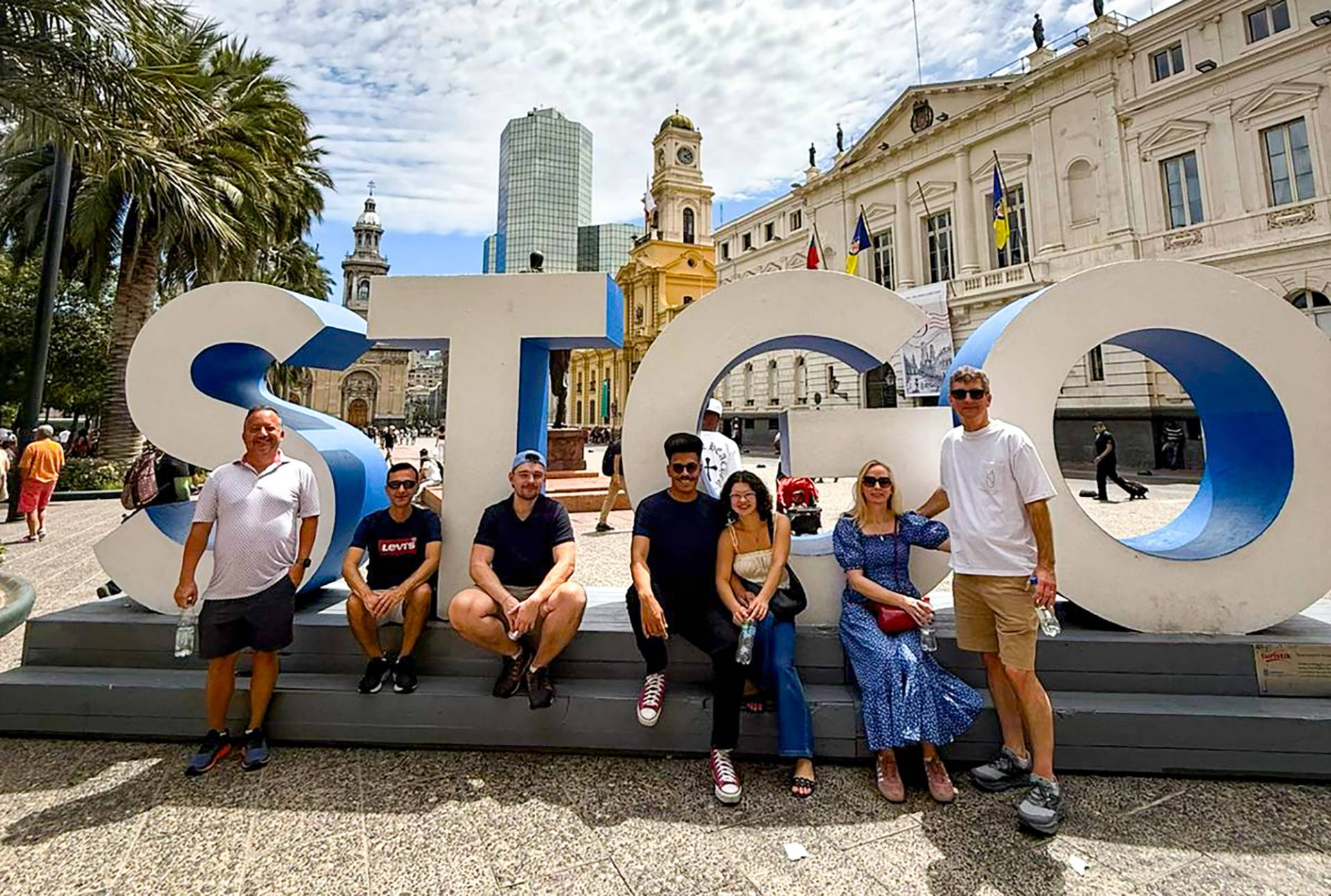 A tour group sitting along the giant STGO letters in the Plaza de Armas, the cathedral behind them