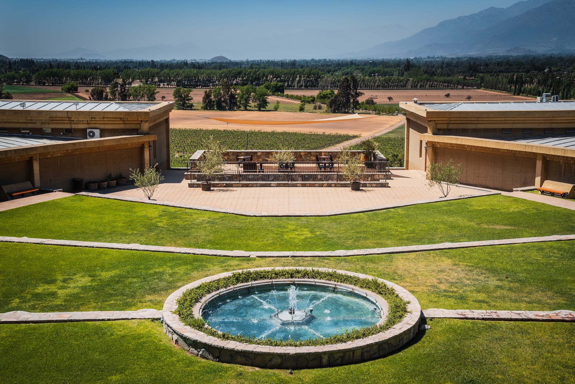 The winery’s manicured gardens and round fountain, framed by vineyard rows and mountains