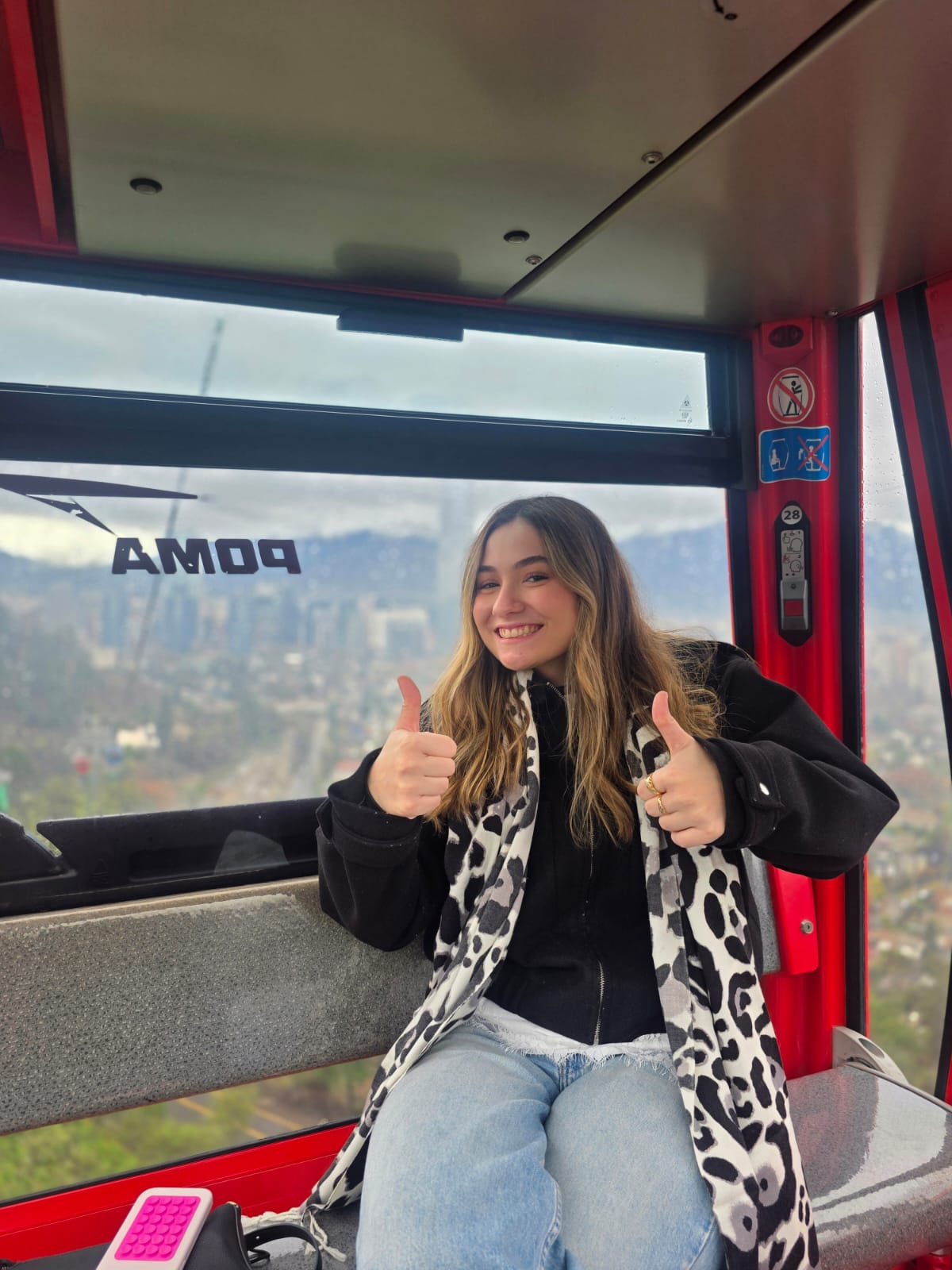 A woman giving a thumbs up inside a cable car cabin marked "POMA"