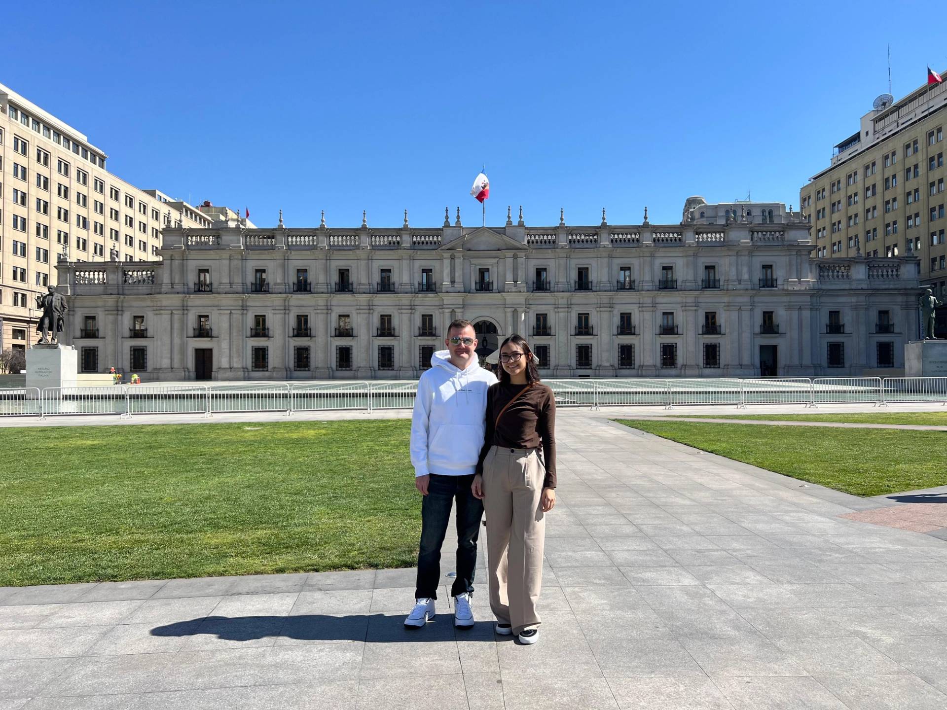 Two travellers standing together on the empty plaza in front of La Moneda palace on a clear day