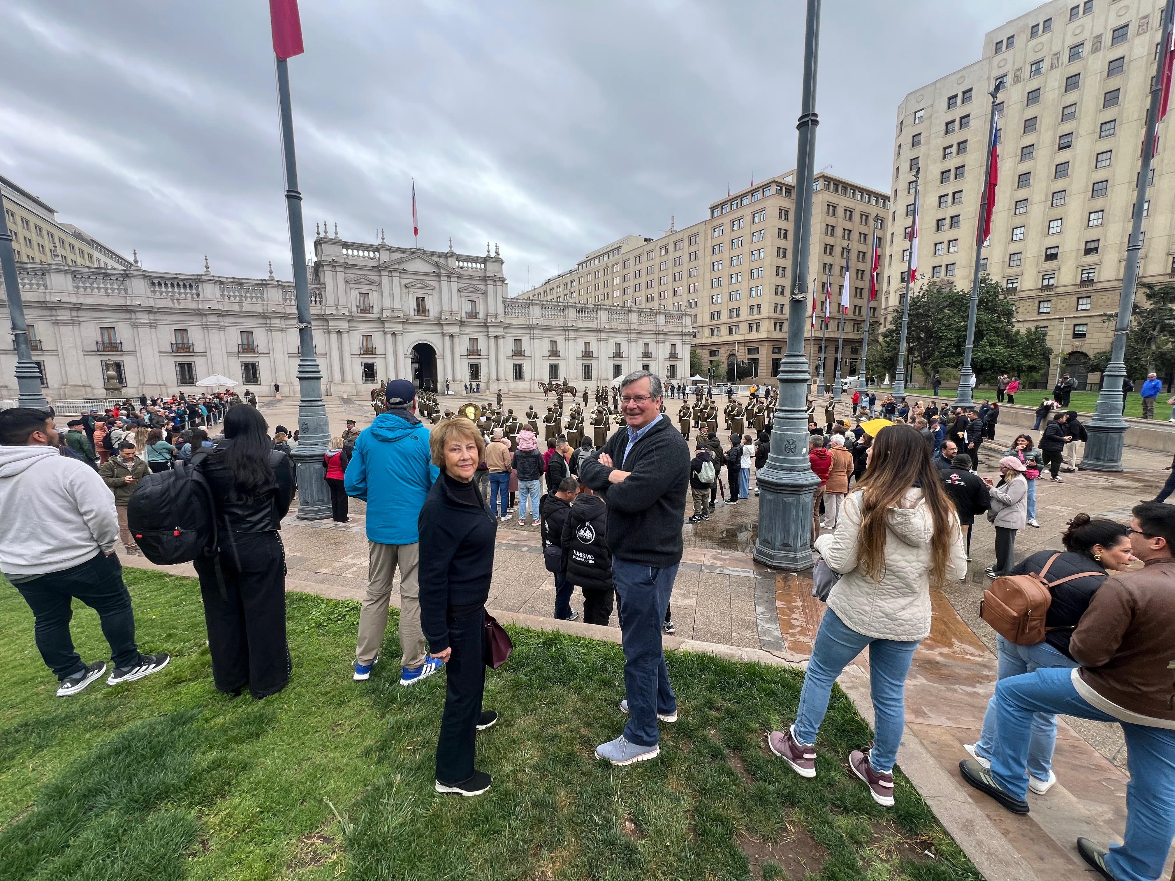 Tourists standing on the grass watching the guard formation in front of La Moneda palace