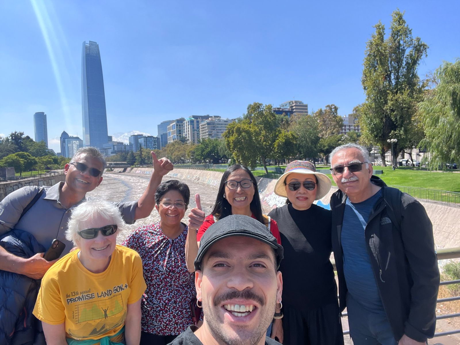 A group posing together in a riverside park, a modern glass tower rising behind them
