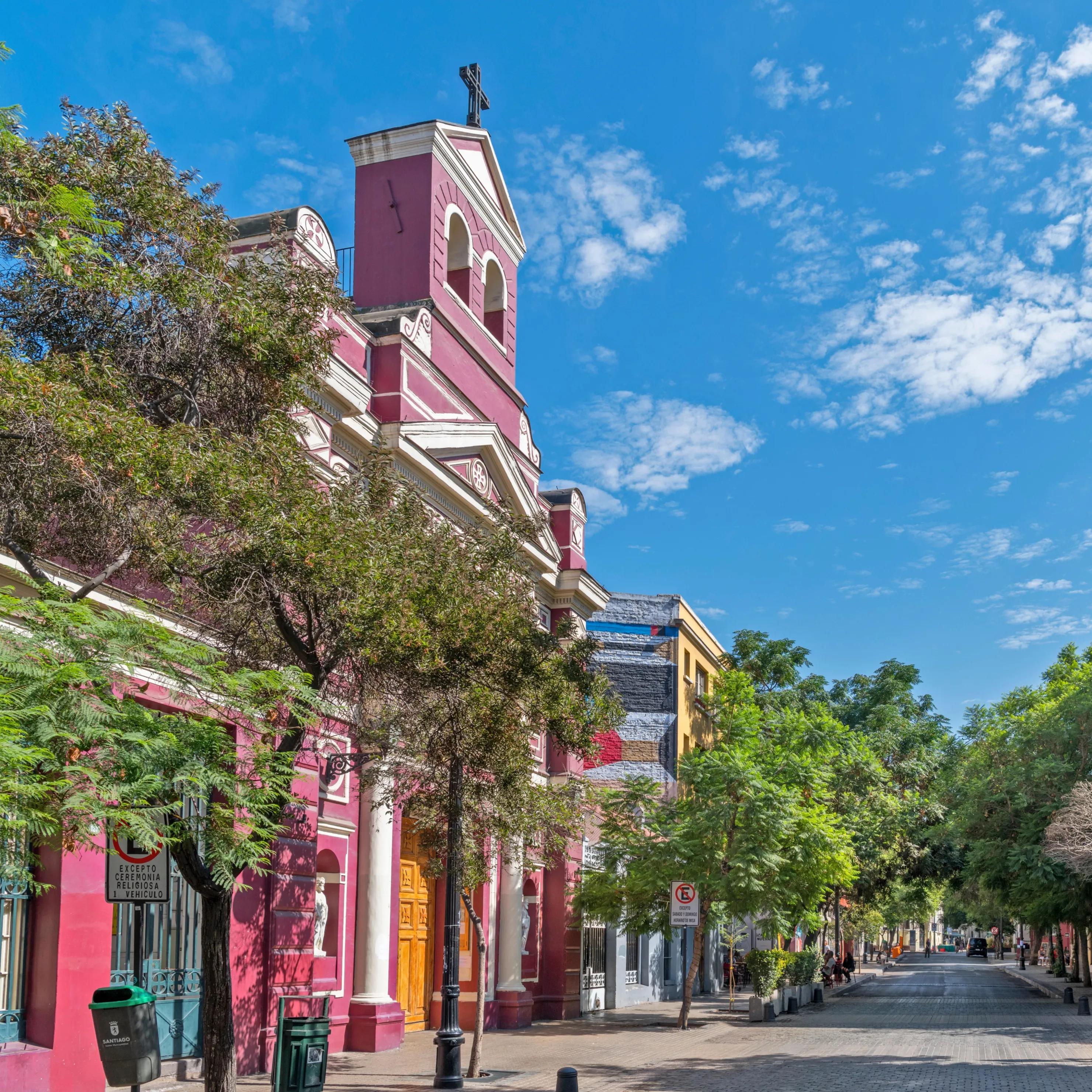 A colorful colonial building with a bell tower on a tree-lined Lastarria street