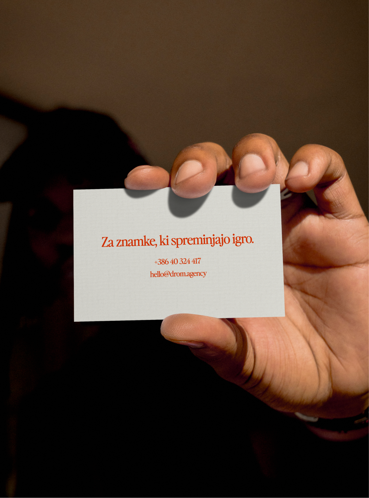 A hand holding up a white DROM card that reads "Za znamke, ki spreminjajo igro." in red.