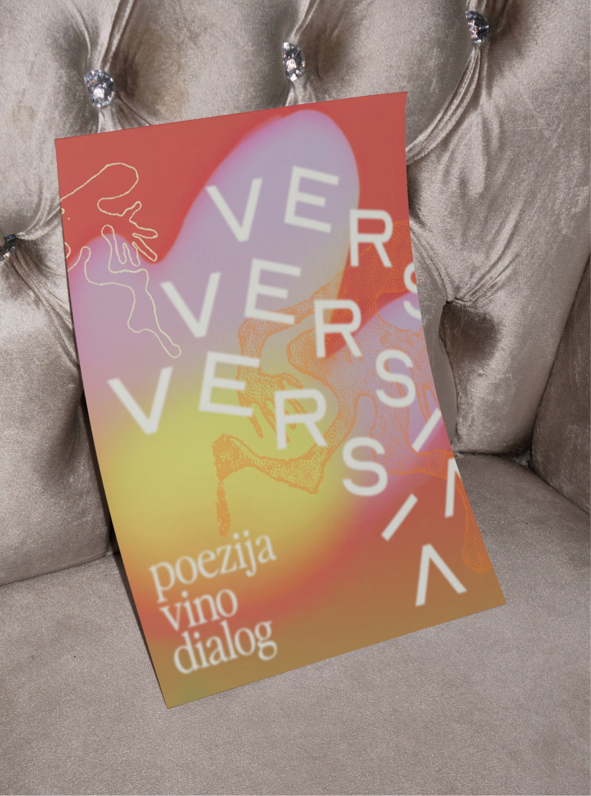 A coral and yellow Versia poster with stacked lettering, propped on a velvet chair.