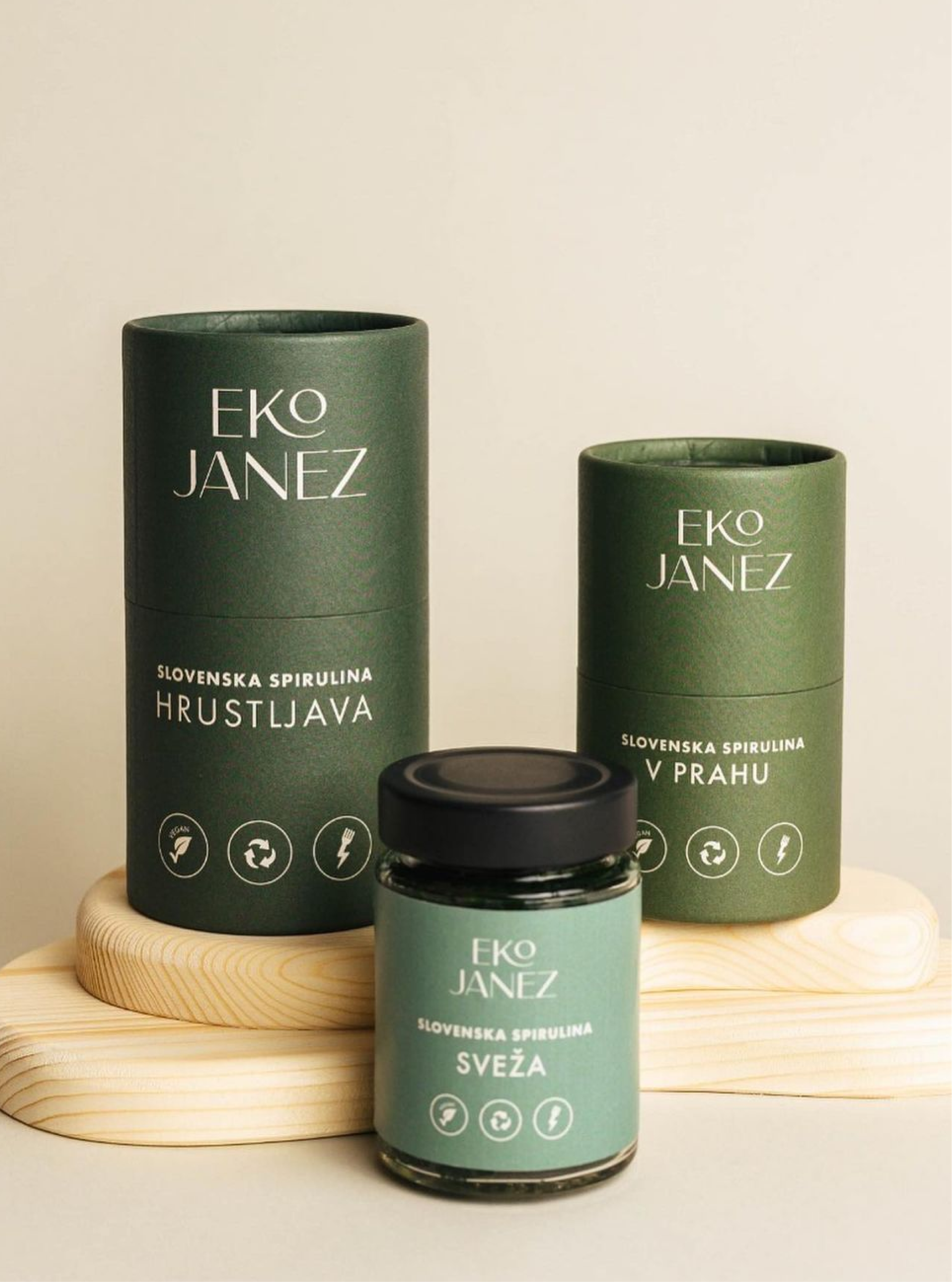 Two Eko Janez tubes and a jar of "Sveža" spirulina on pale wooden stands, against beige.