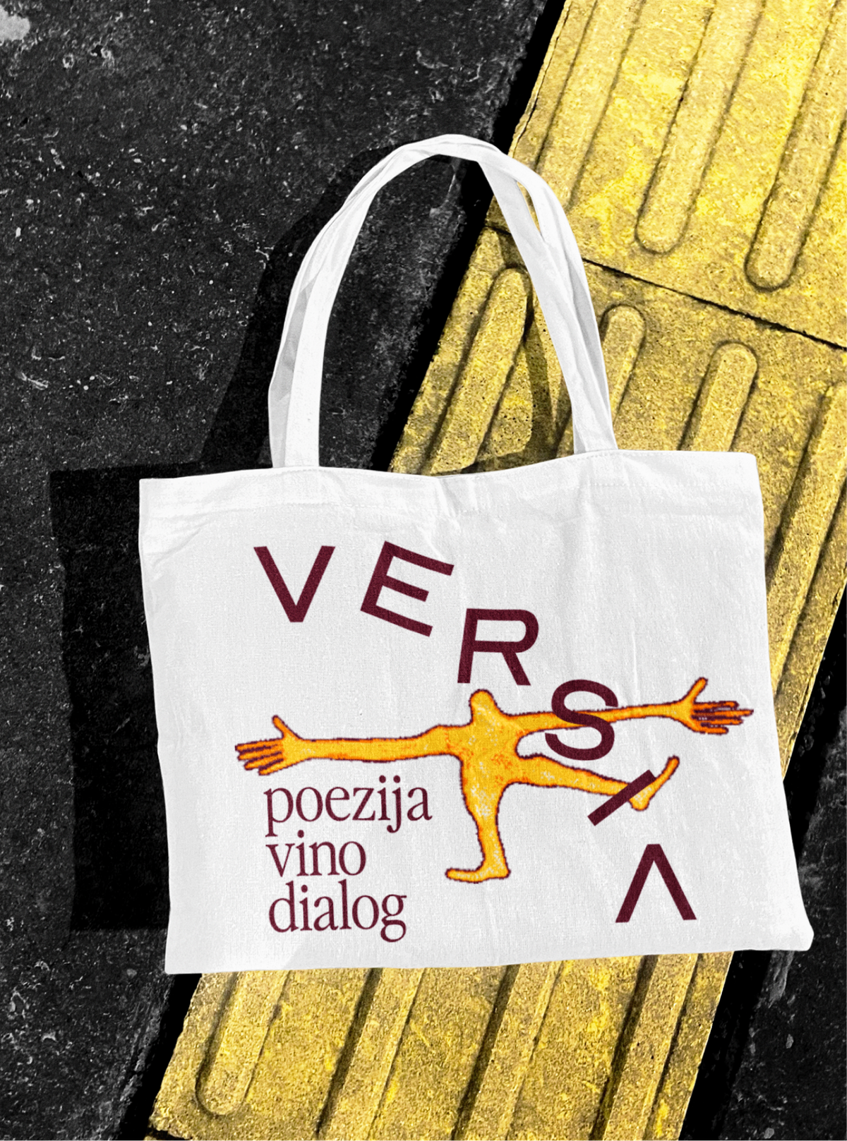 A Versia tote bag with a yellow drawn figure, on a yellow tactile paving stripe.
