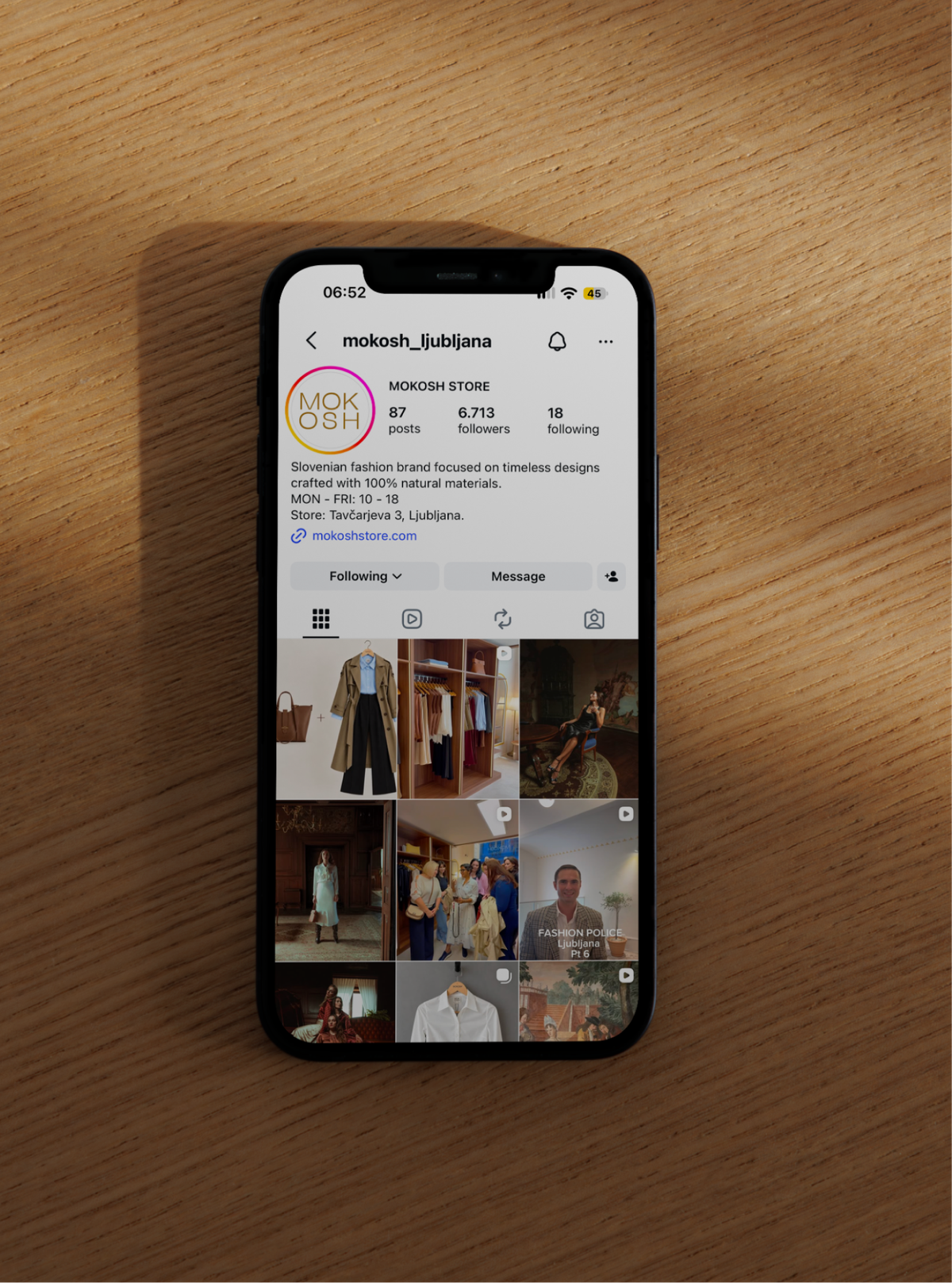 A phone on a wooden table, open on the mokosh_ljubljana Instagram profile of clothing photos.