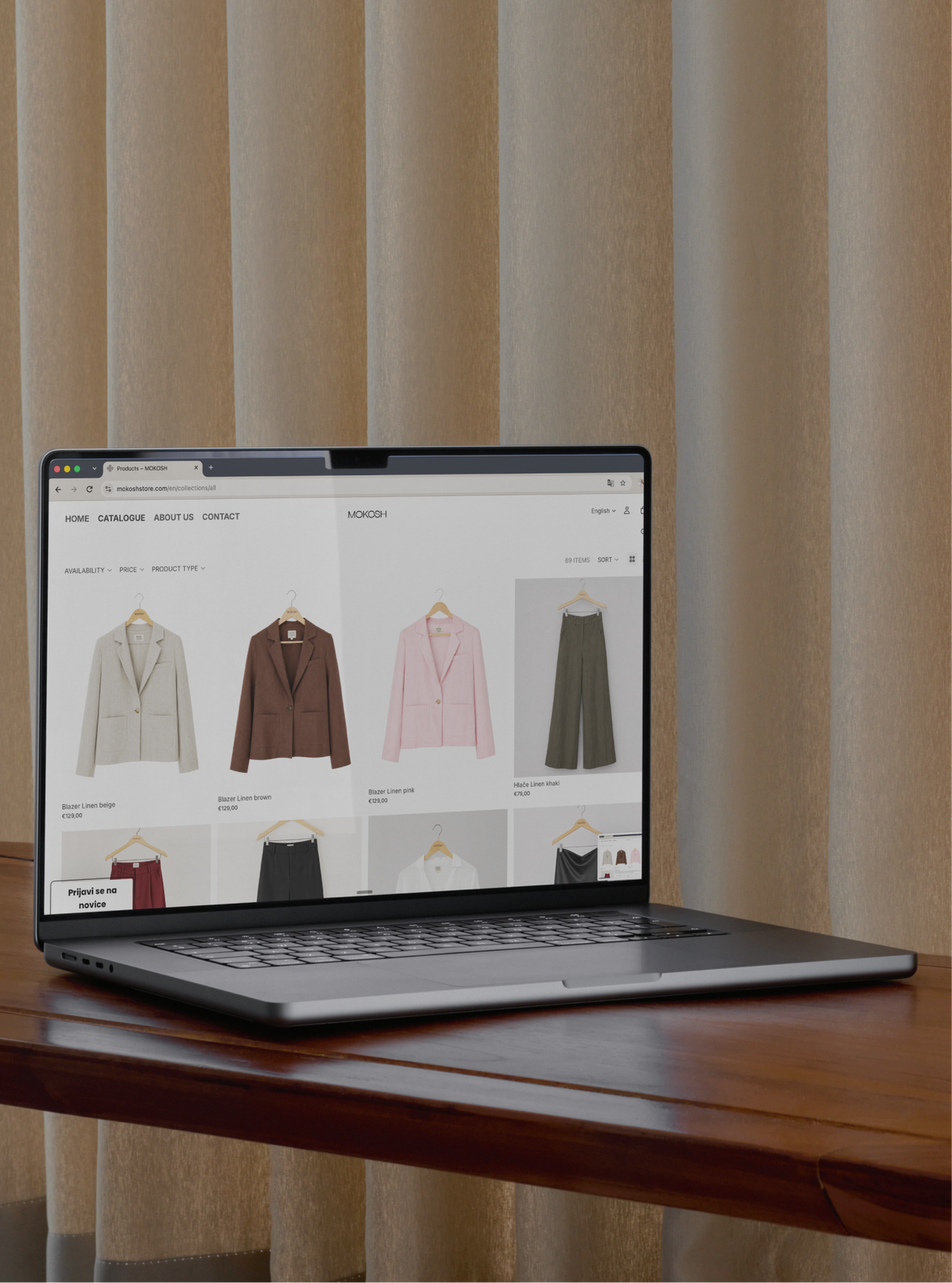 A laptop on a wooden table showing the Mokosh online catalogue of blazers and trousers on hangers.