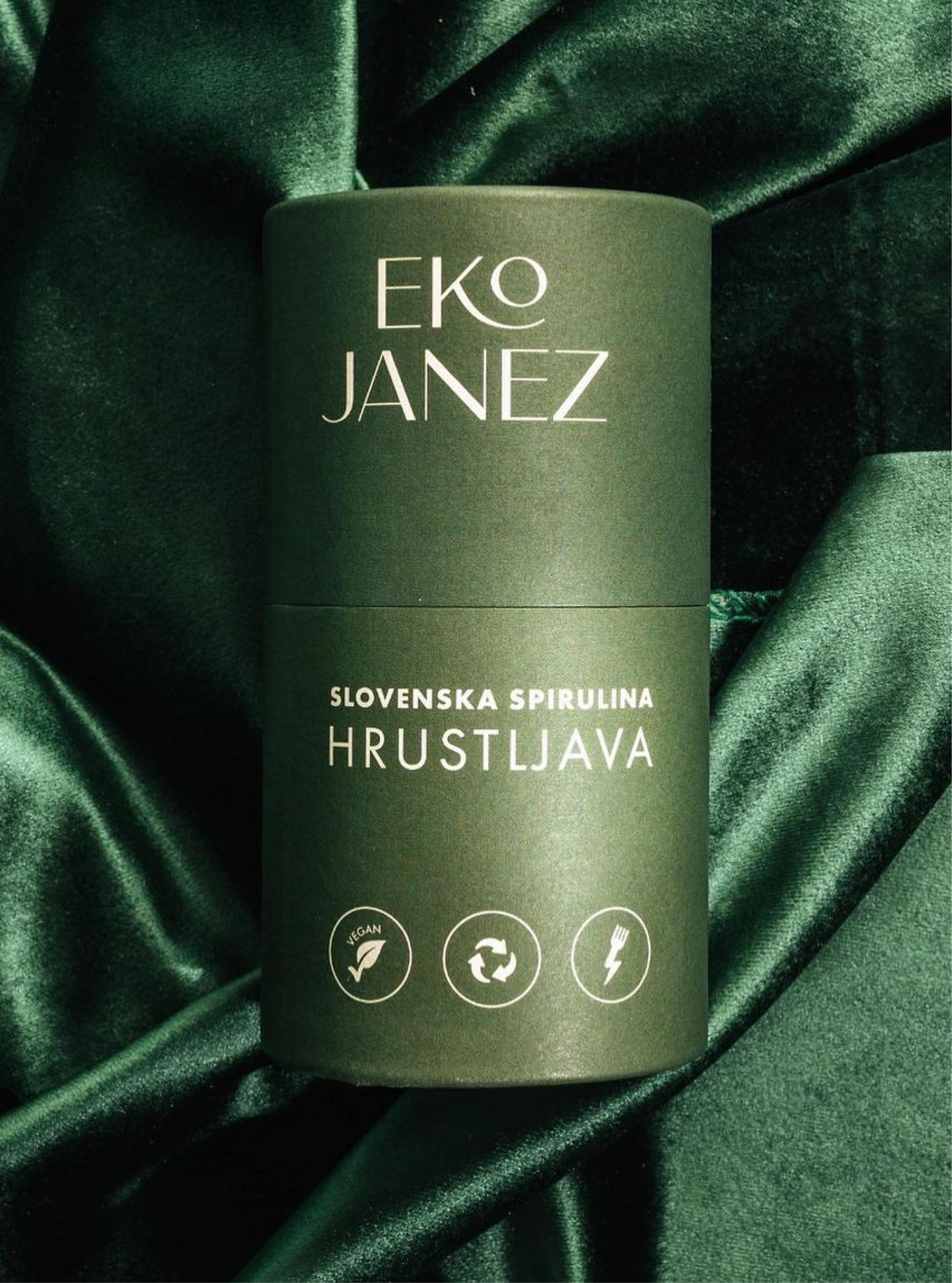 A dark green Eko Janez tube of "Slovenska spirulina hrustljava" laid on folds of green velvet.