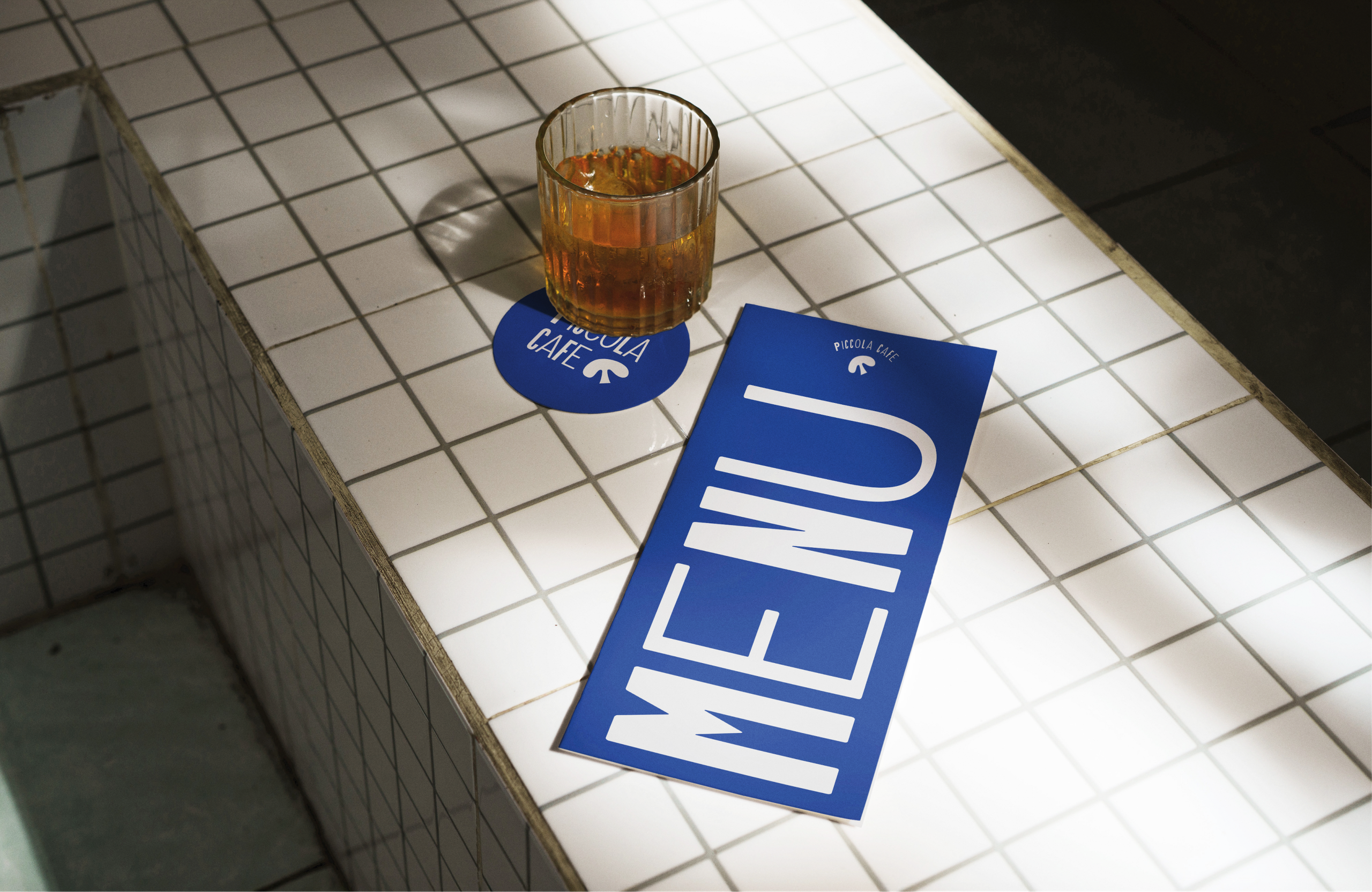 A blue menu card and a coaster beside a glass on a white-tiled counter.