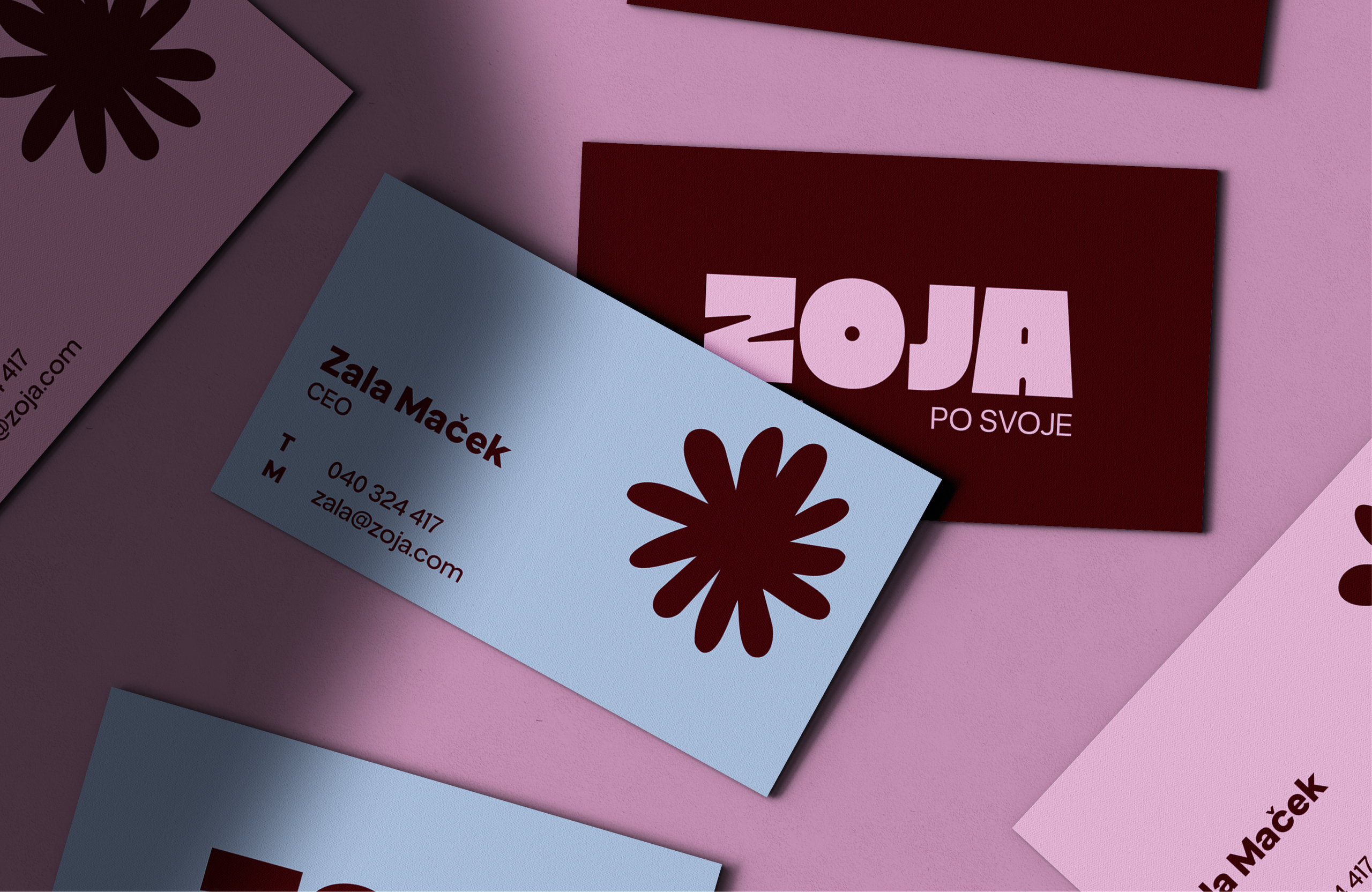 Zoja business cards in pale blue, pink and burgundy with a dark flower mark, scattered on pink.