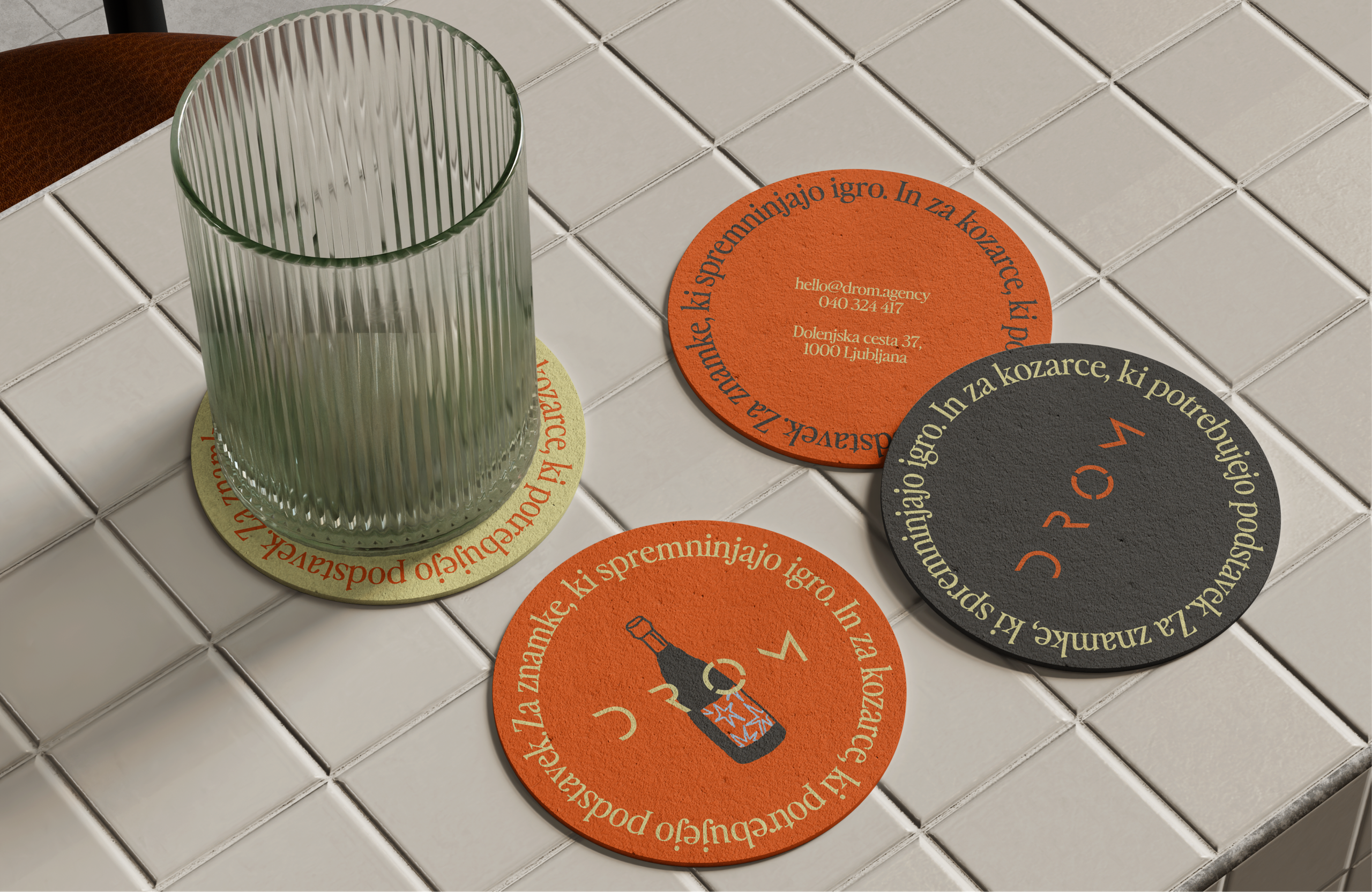 DROM coasters in orange, charcoal and yellow, ringed with lettering, and a ribbed glass on white tiles.