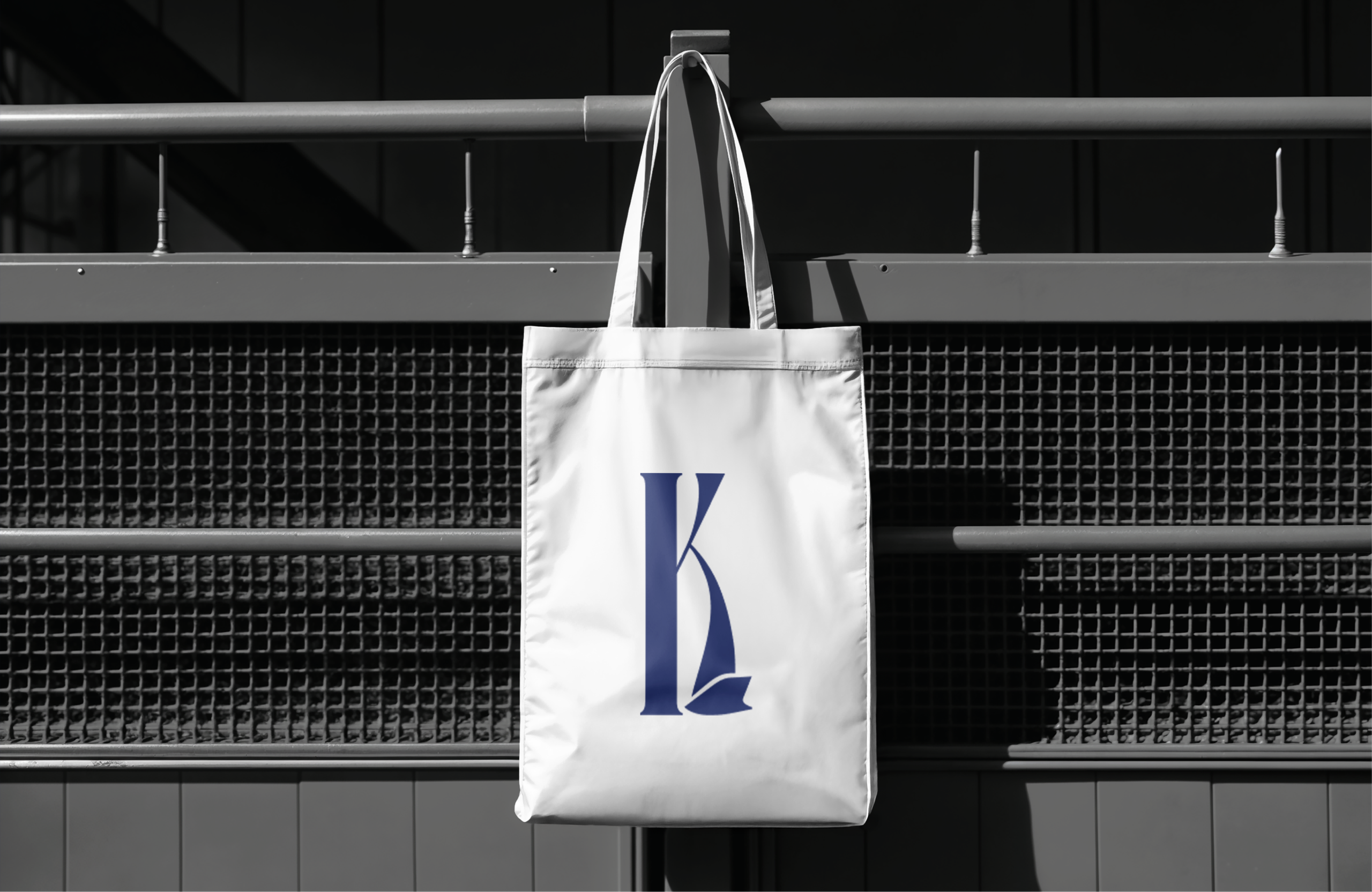 A white tote bag with the navy K monogram, hanging from a railing.