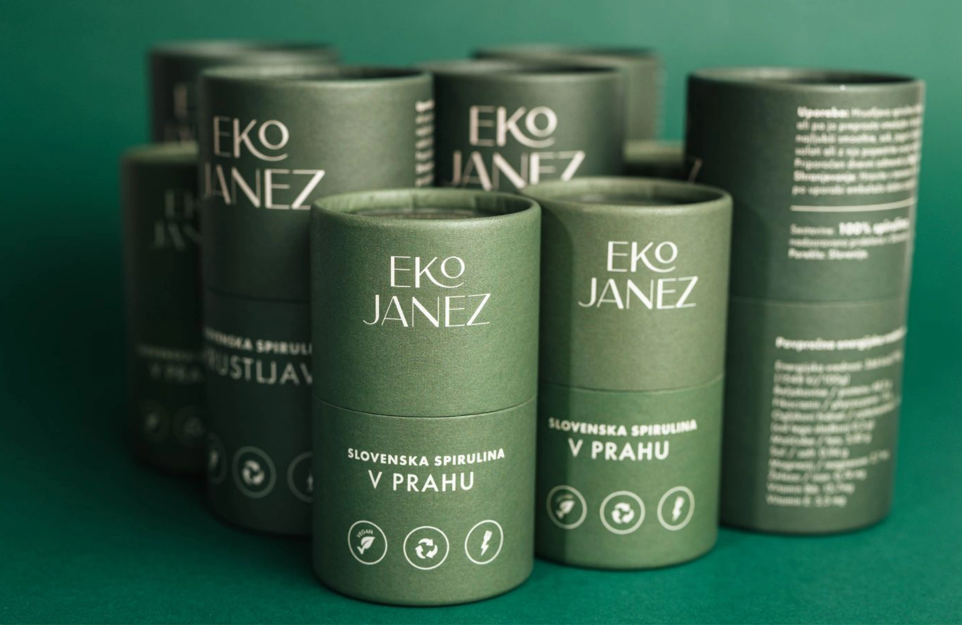 A cluster of dark green Eko Janez tubes of "Slovenska spirulina v prahu" on a green background.