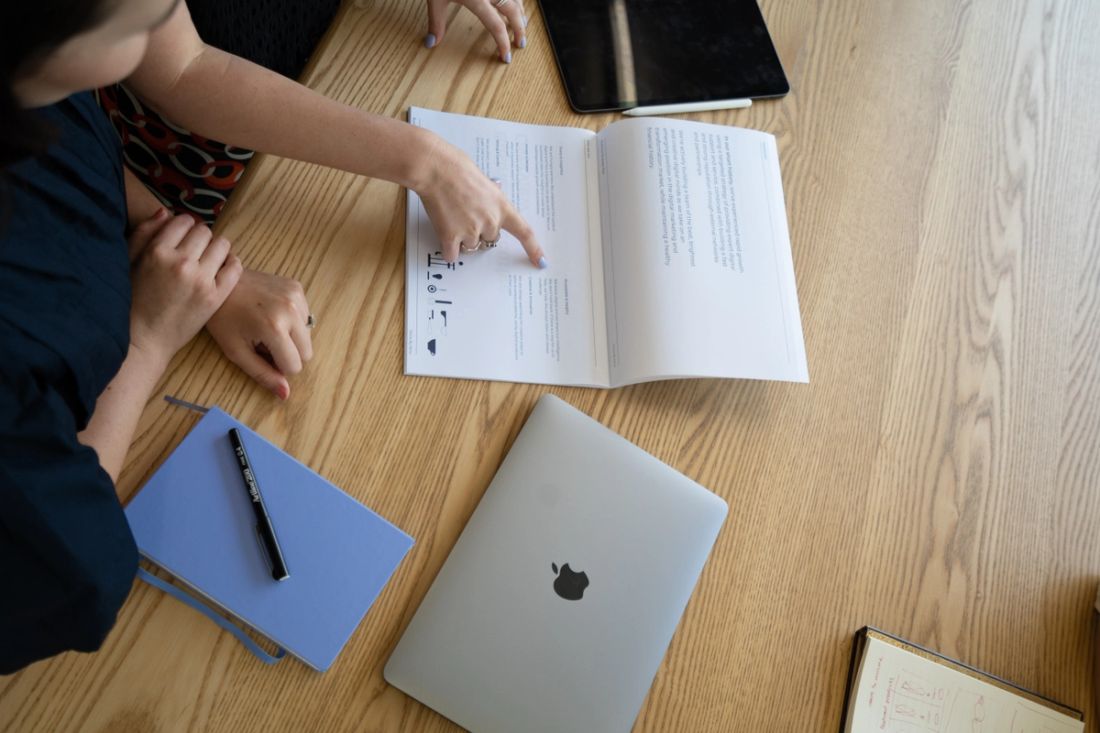 Two people reading a printed marketing strategy document beside a laptop and notebook