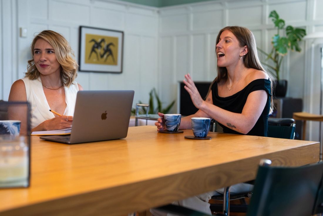 Two Done By Nine marketers talking over an open laptop and notes at the studio table
