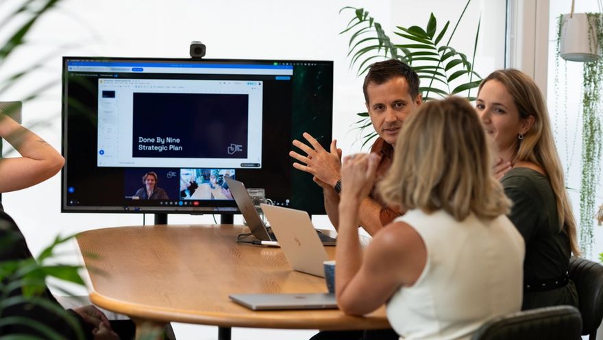 The Done By Nine team around a table, talking through the strategic plan on the screen behind them