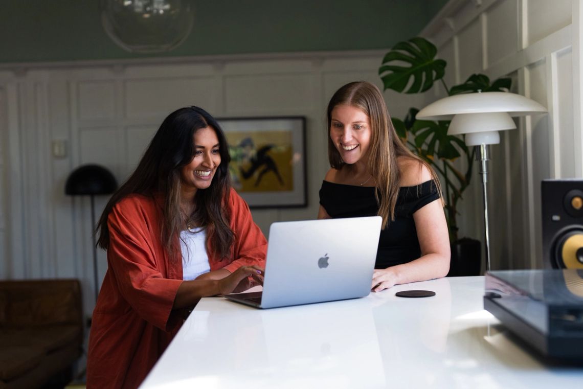 One person typing on a laptop while a colleague watches the screen change beside her