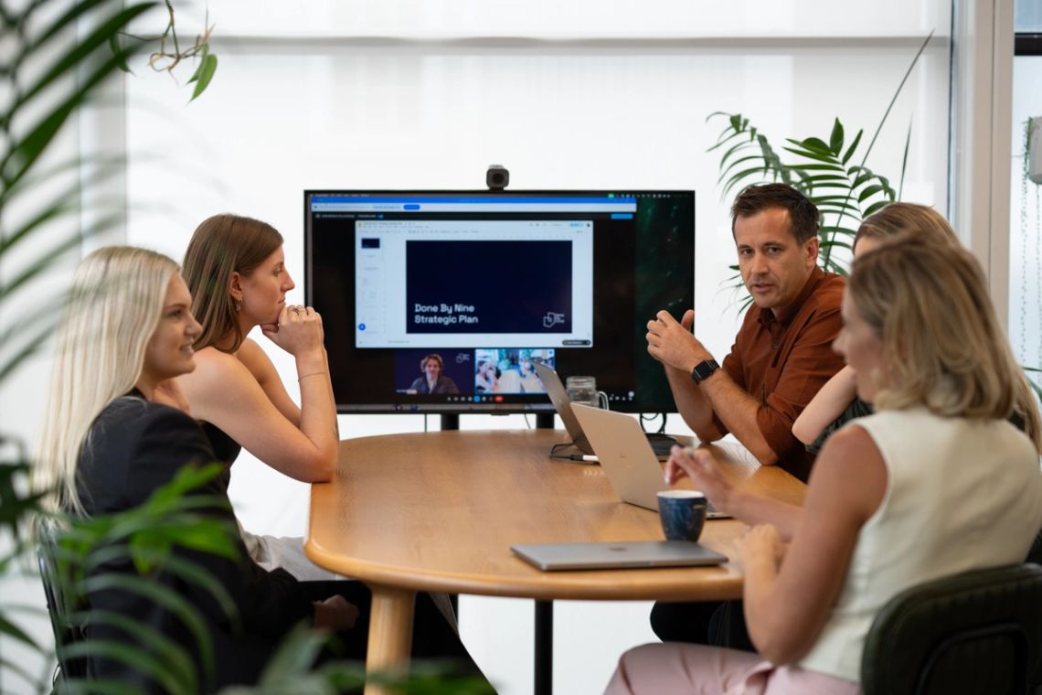 The Done By Nine team around a table watching a strategy deck on the meeting-room screen