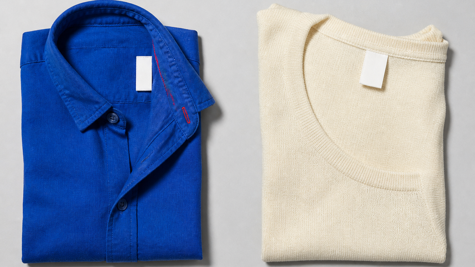 A cobalt shirt and an ivory knit top lie side by side on a cool grey studio surface, each showing a plain white care-label area without readable symbols or instructions.