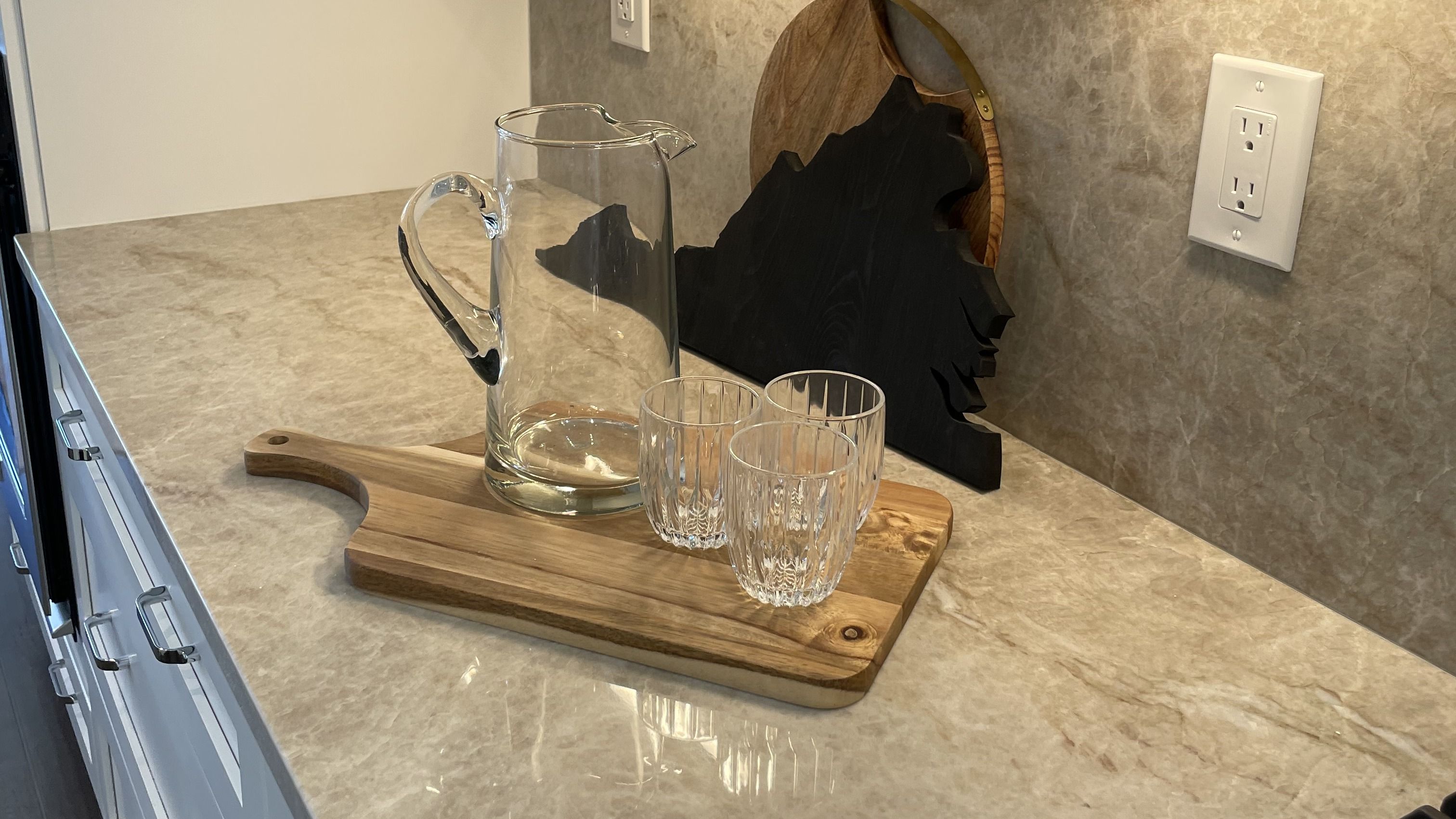 A glass pitcher and crystal tumblers on a Virginia-shaped cutting board, on a polished marble counter