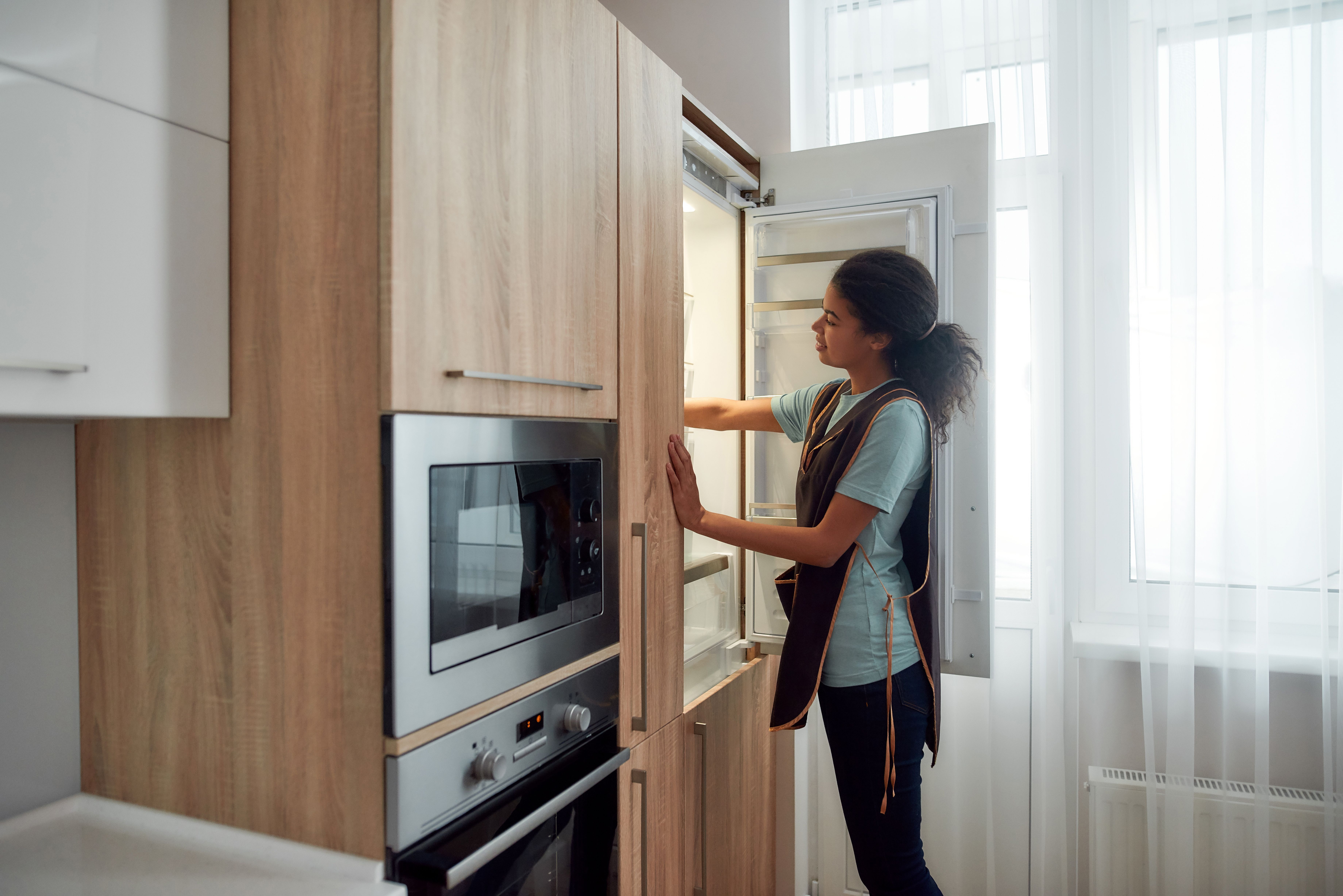 A cleaner in an apron wiping down the inside of an open refrigerator