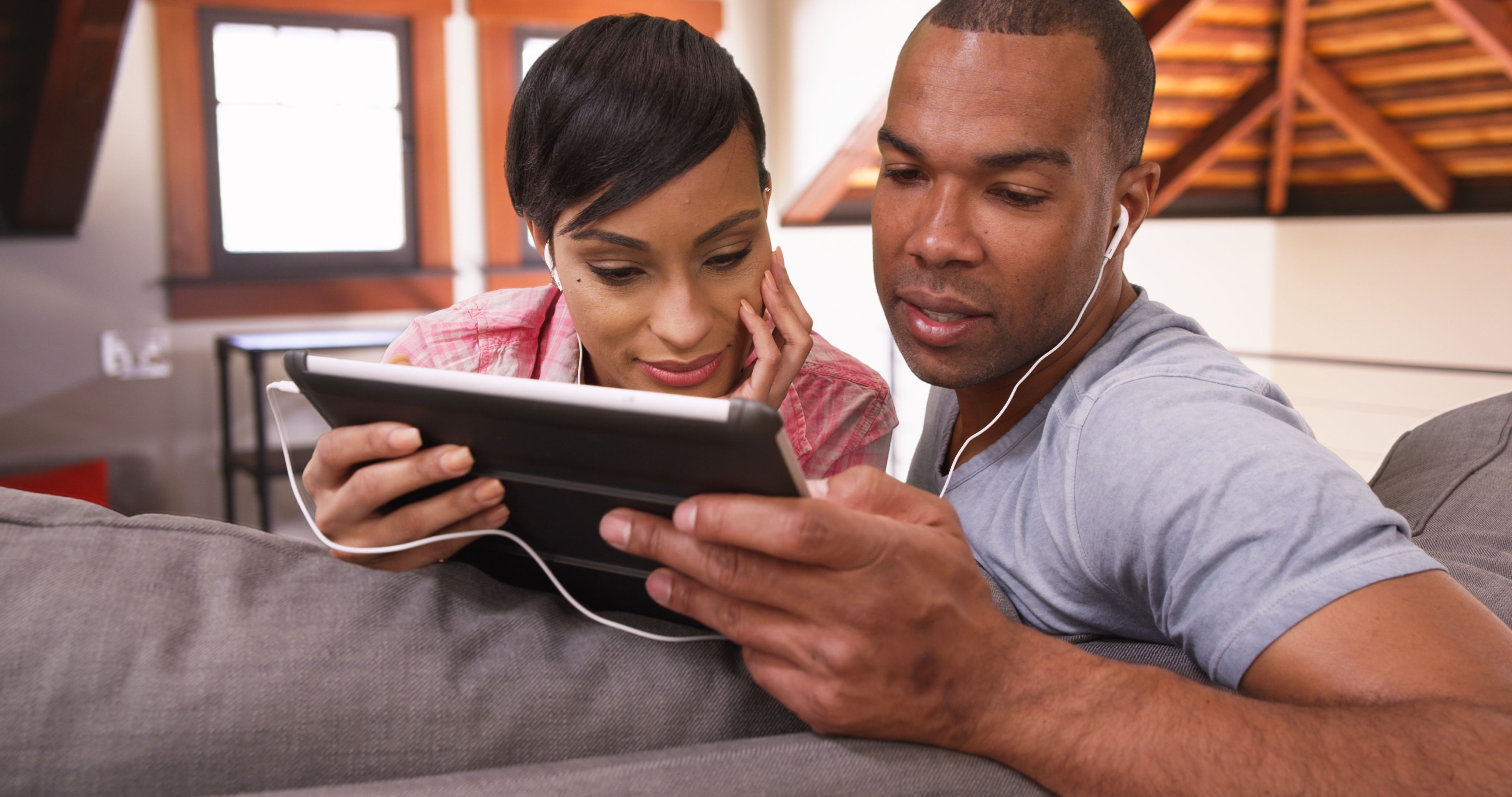 A couple at home looking at a tablet together on the sofa