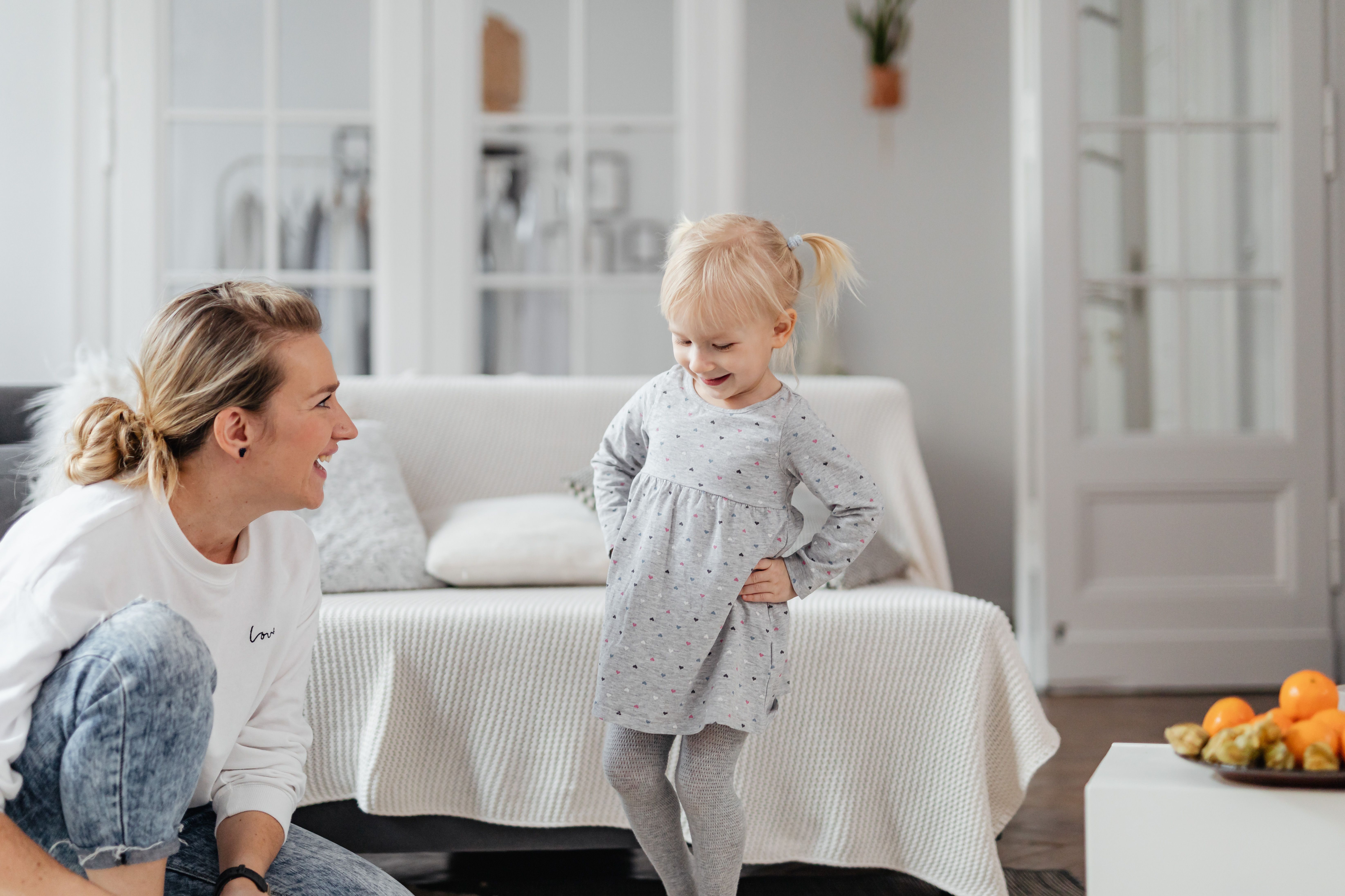 A mother and her young daughter laughing together in a bright, tidy living room